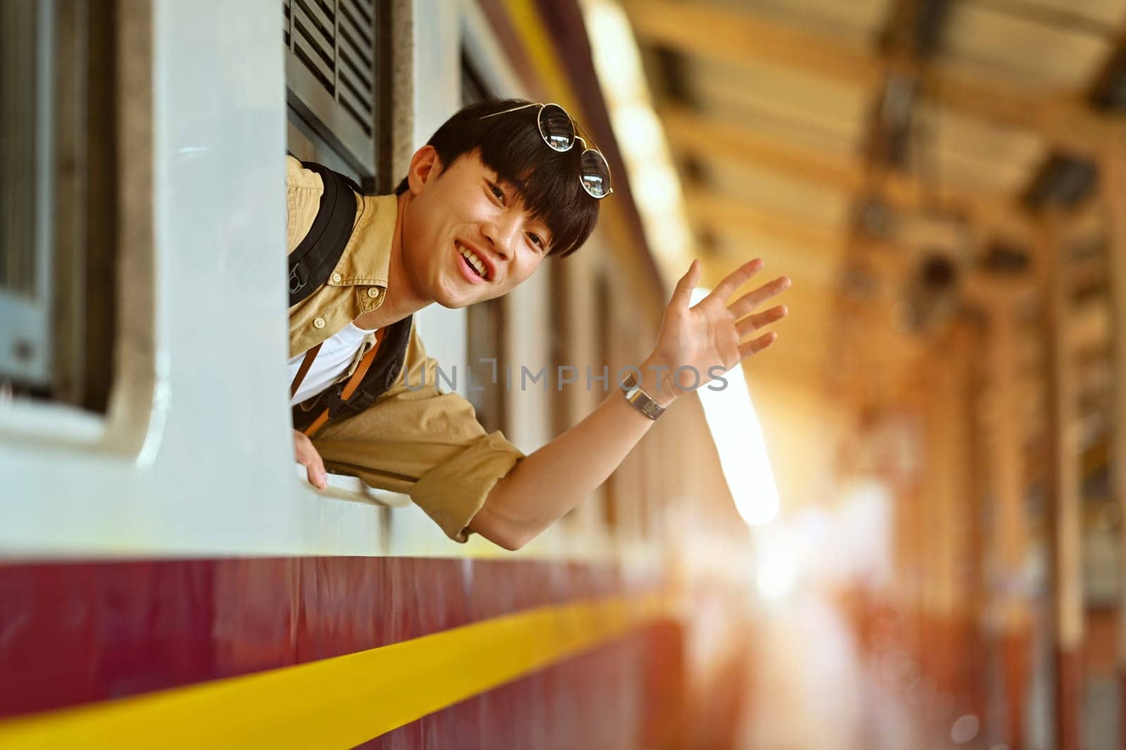 Happy young Asian man waving hand to friend through train window before leaving by prathanchorruangsak