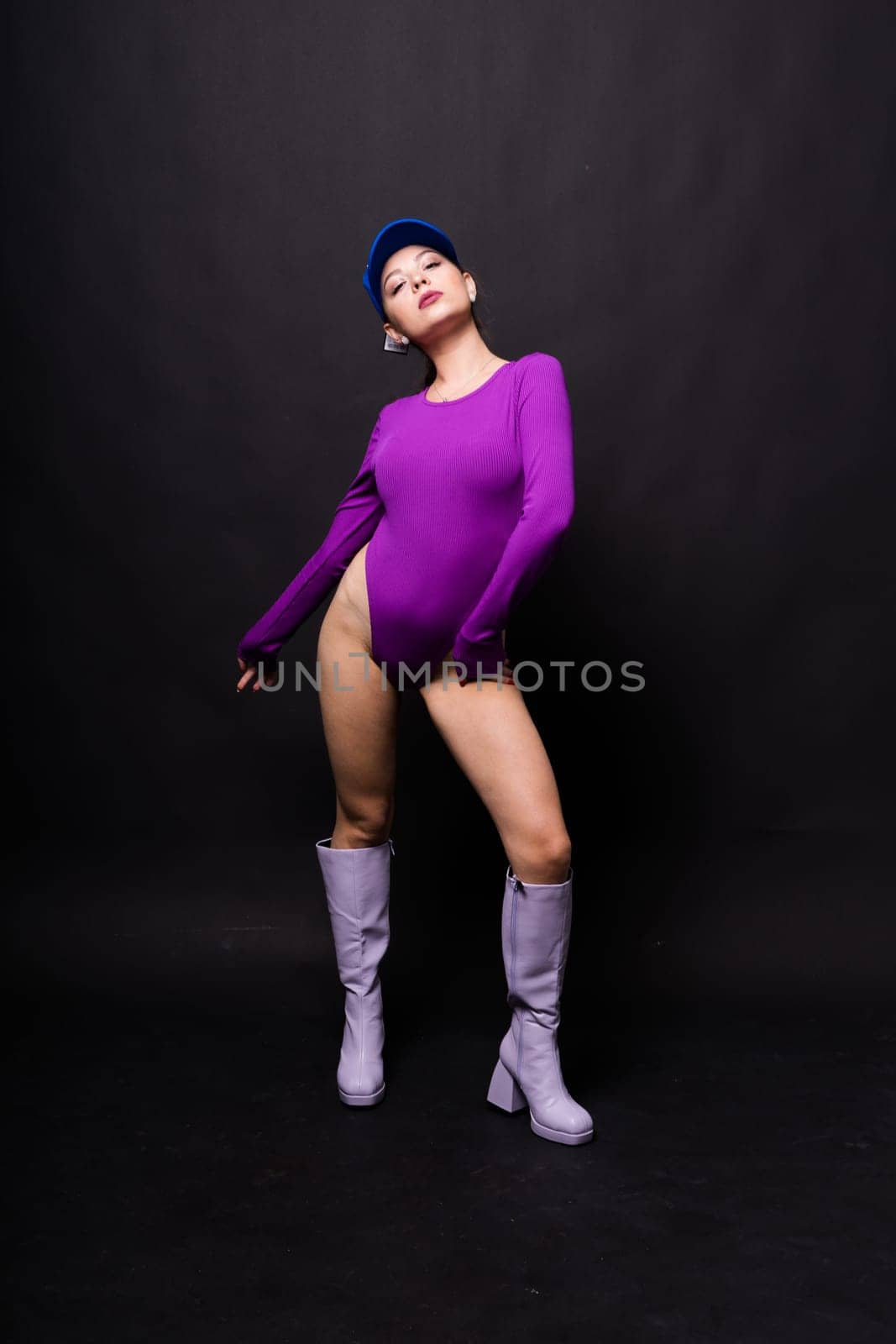 Slender seductive brunette female in violet bodysuit against a dark background.