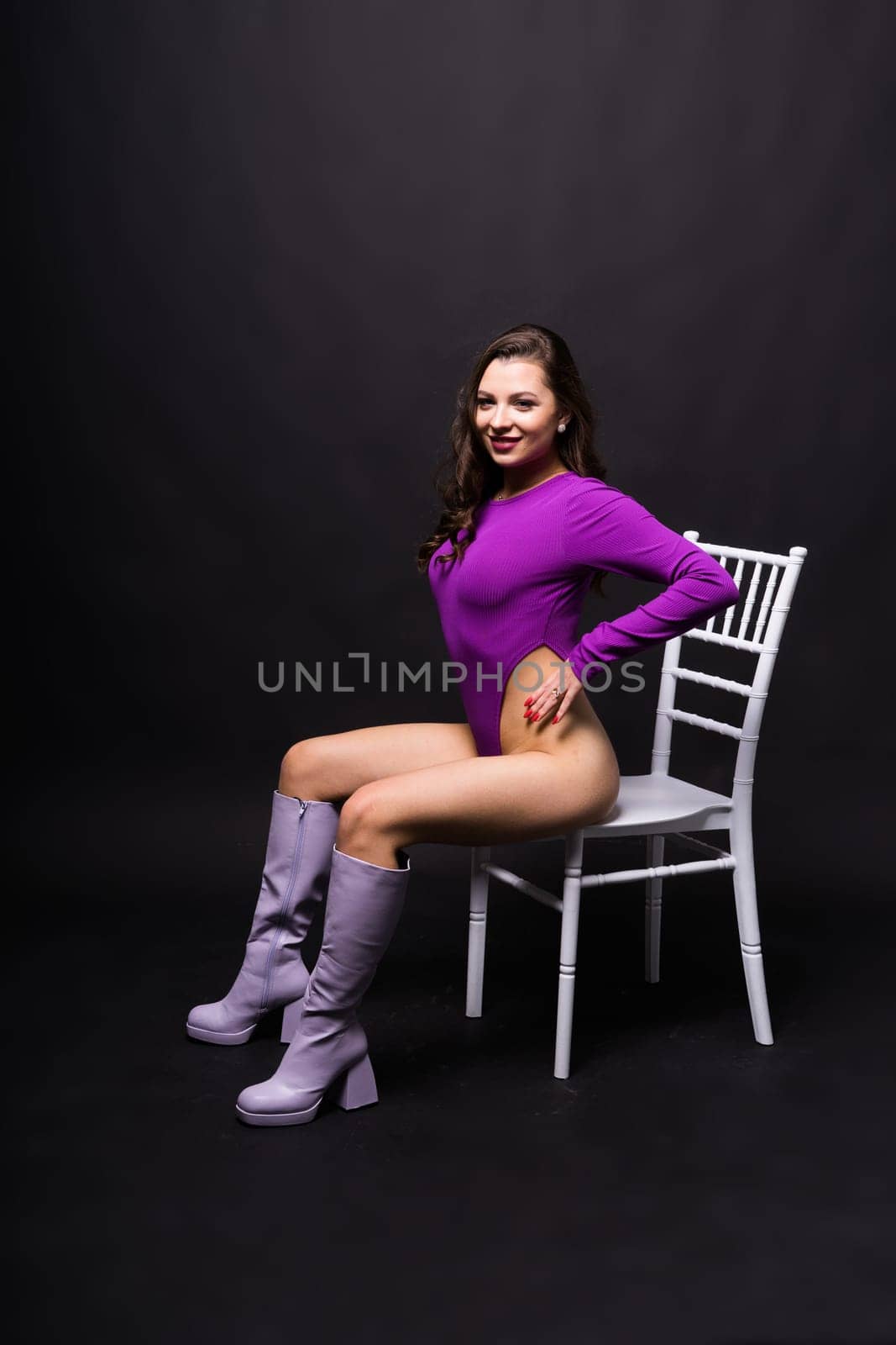 Slender seductive brunette female in violet bodysuit against a dark background.