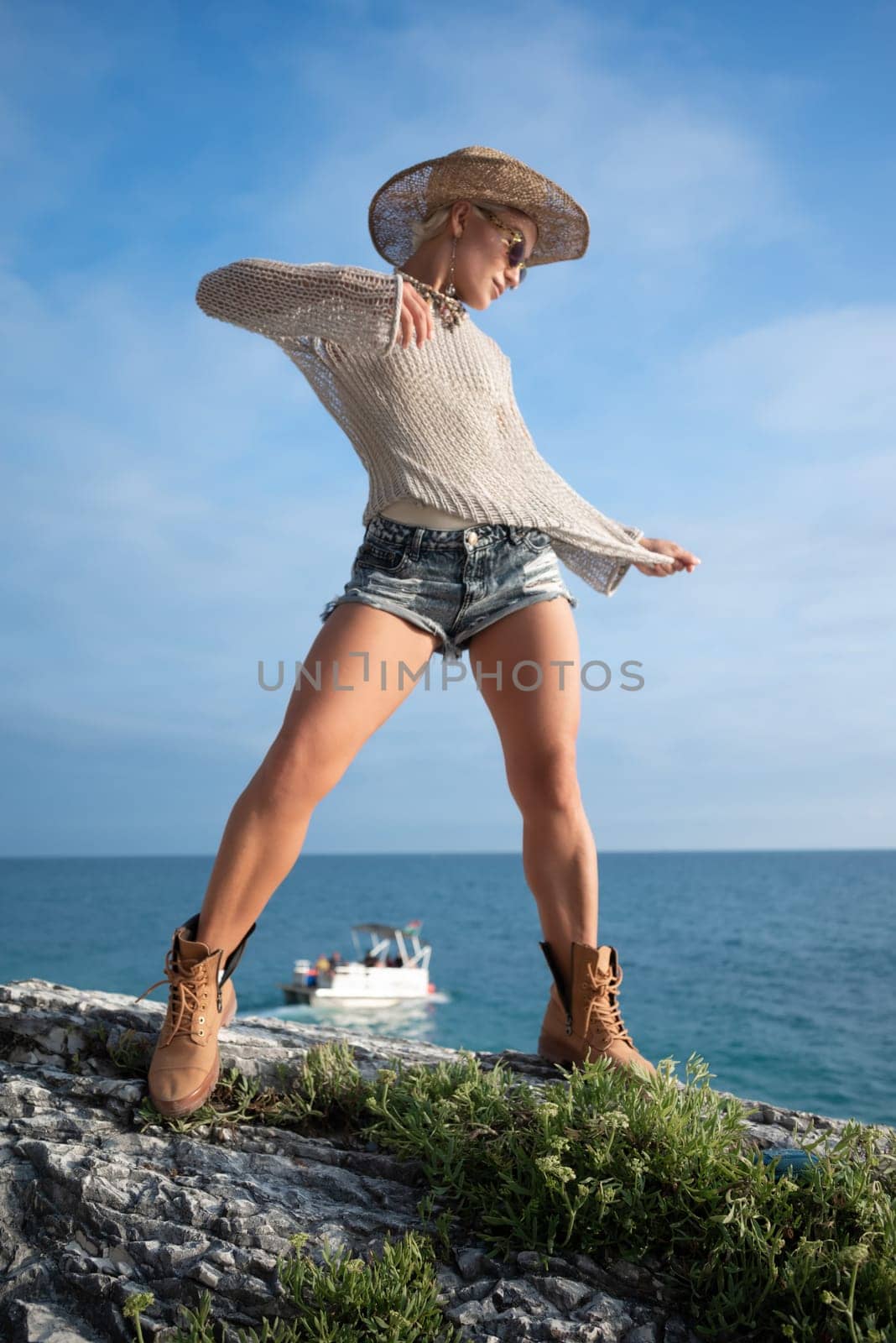 sexy girl in stylish fashionable summer clothes, cowboy hat and cool boots, posing freely on white rocks against the background of the sea by Rotozey