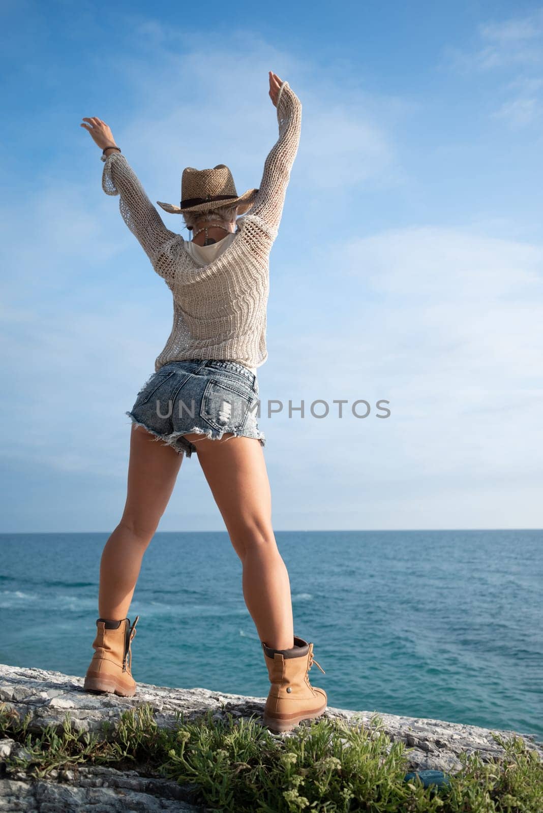 sexy girl in stylish fashionable clothes, cowboy hat and cool boots, posing freely on white rocks against the background of the sea