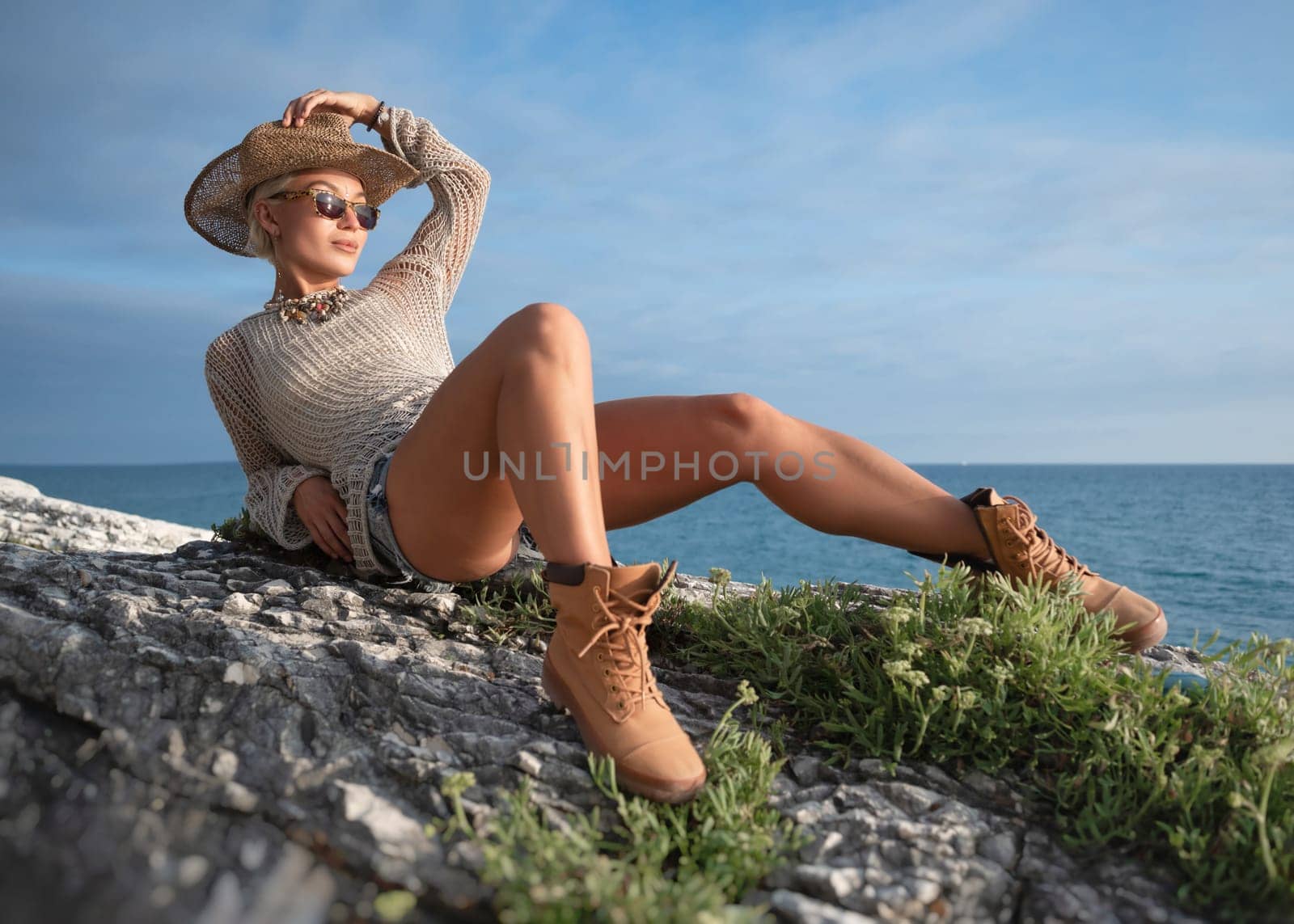 sexy girl in stylish fashionable summer clothes, cowboy hat and cool boots, posing freely on white rocks against the background of the sea by Rotozey