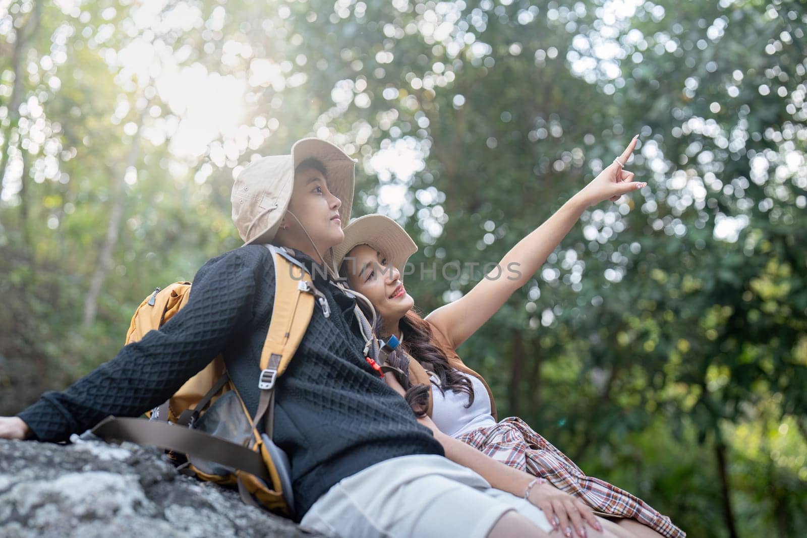 Cheerful romantic lesbian couple traveler with backpacks and siting relaxing while hiking in the mountains in summer by nateemee