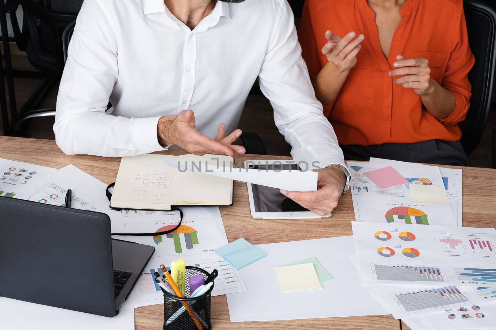 Two young businesspeople smiling while working with wireless technology in a modern workspace.