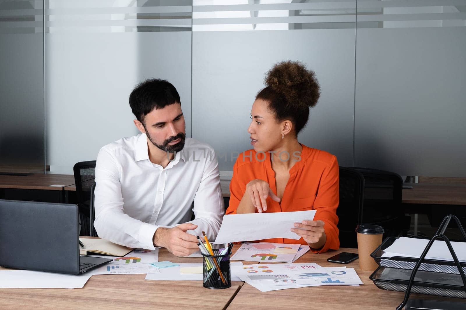 Two young businesspeople smiling while working with wireless technology in a modern workspace.