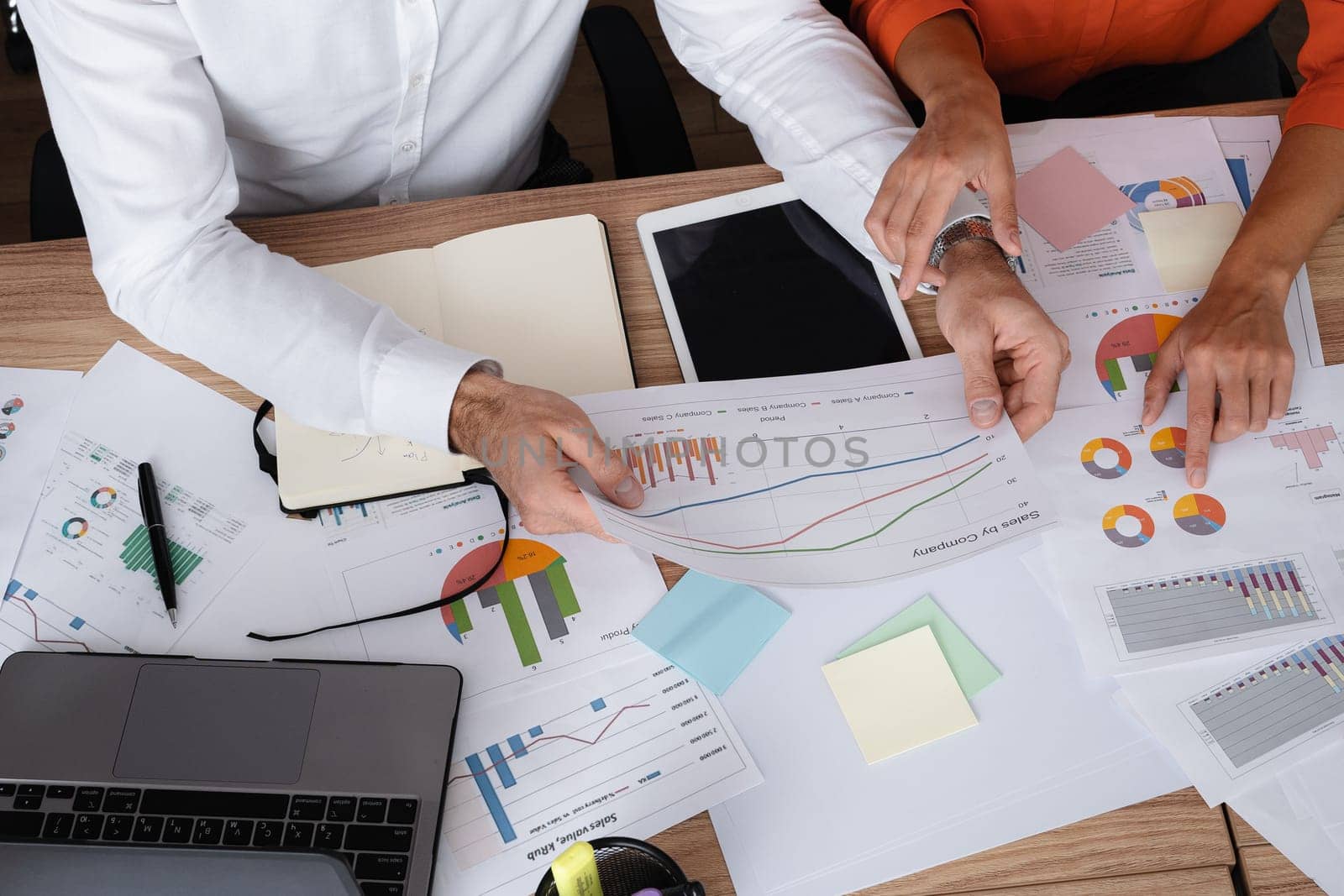 Two young businesspeople smiling while working with wireless technology in a modern workspace.