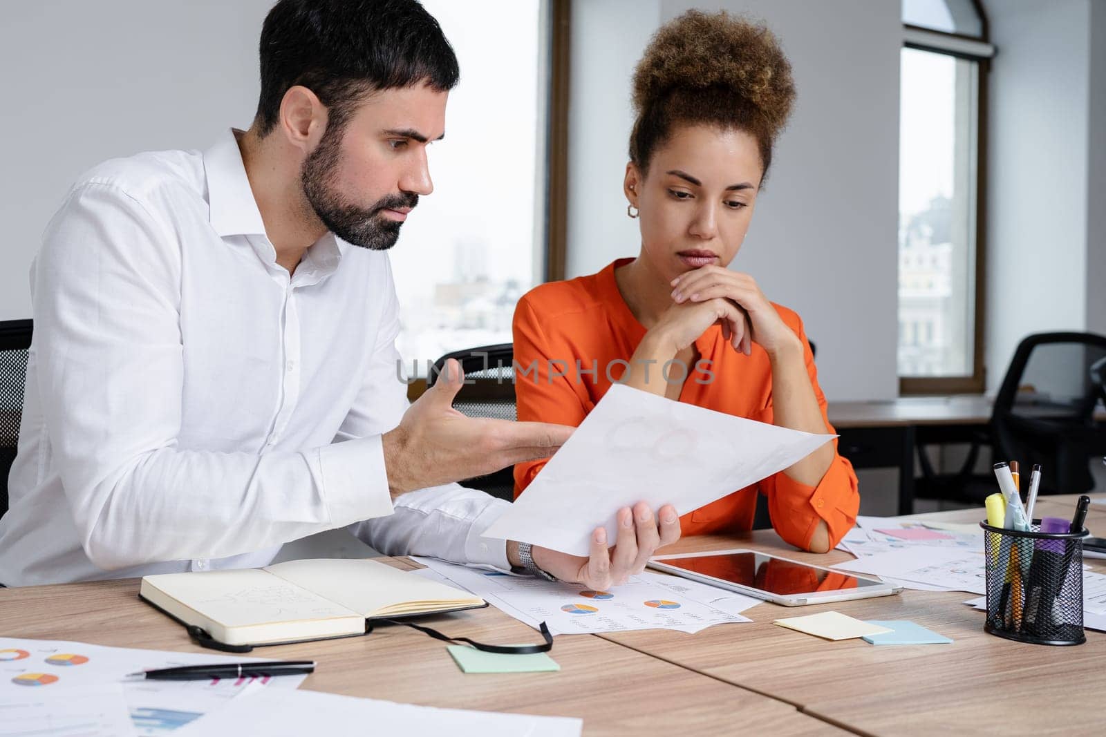 Two young businesspeople smiling while working with wireless technology in a modern workspace.