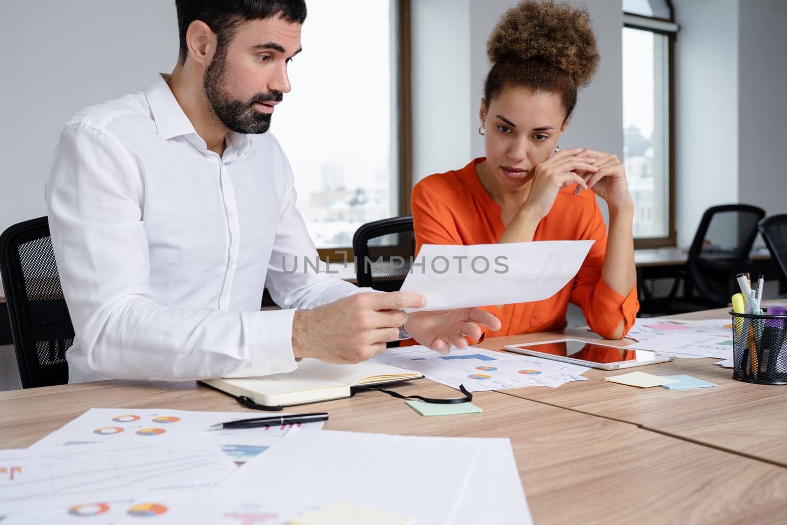 Two young businesspeople smiling while working with wireless technology in a modern workspace.