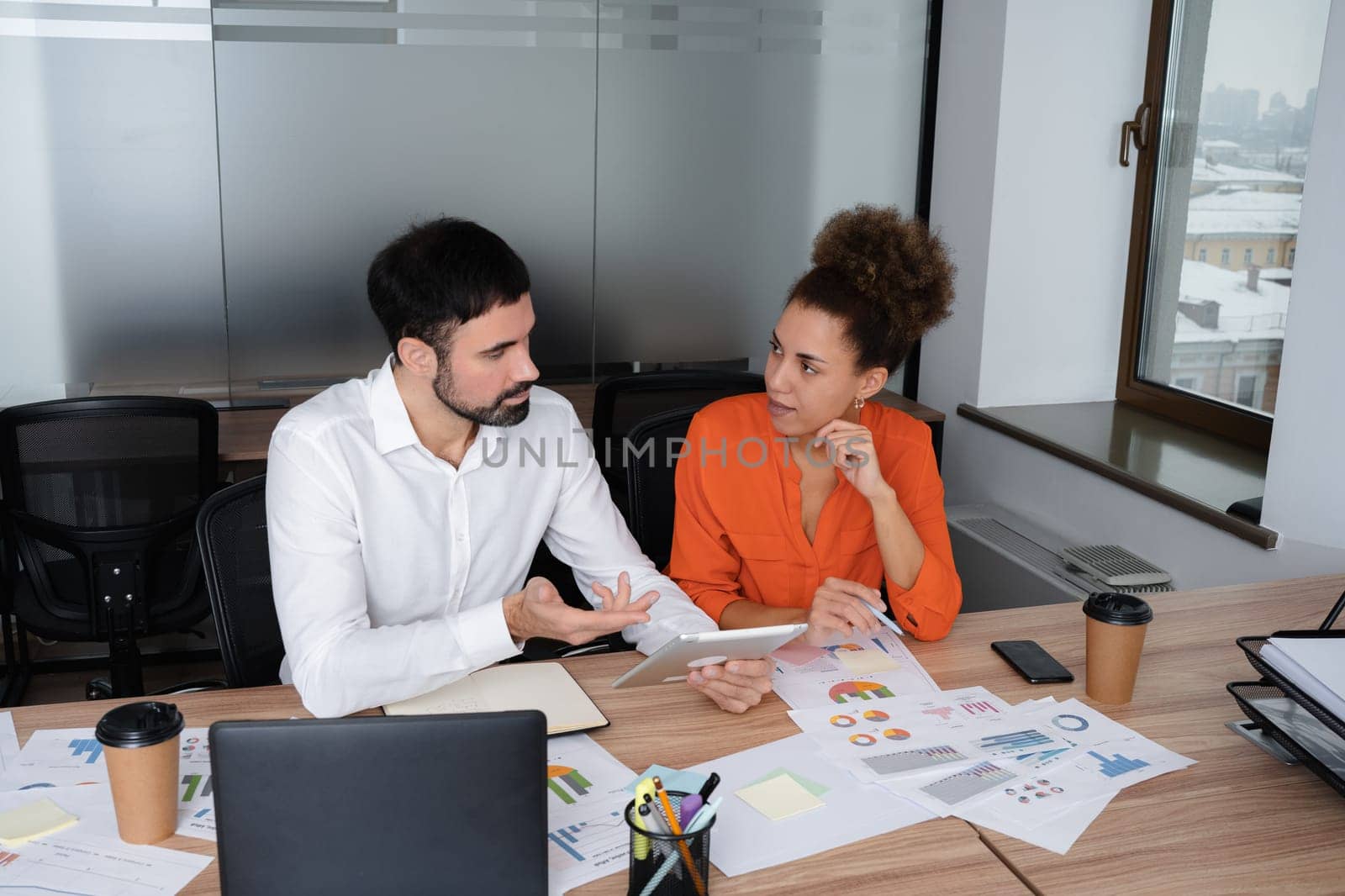 Two young businesspeople smiling while working with wireless technology in a modern workspace.