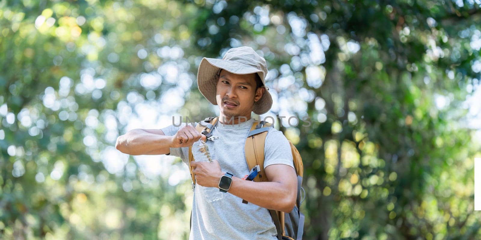 Young man backpacker traveling alone in forest. Attractive male traveler drinking water while walking in nature wood during holiday vacation trip by itchaznong