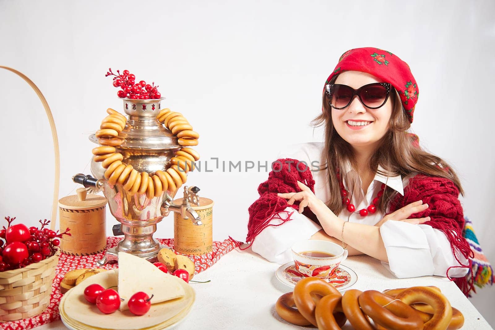 A fashionable modern girl in stylized folk clothes at a table with a samovar, bagels and tea for the Orthodox holiday of Maslenitsa and Easter. Funny photo shoot for a young woman by keleny