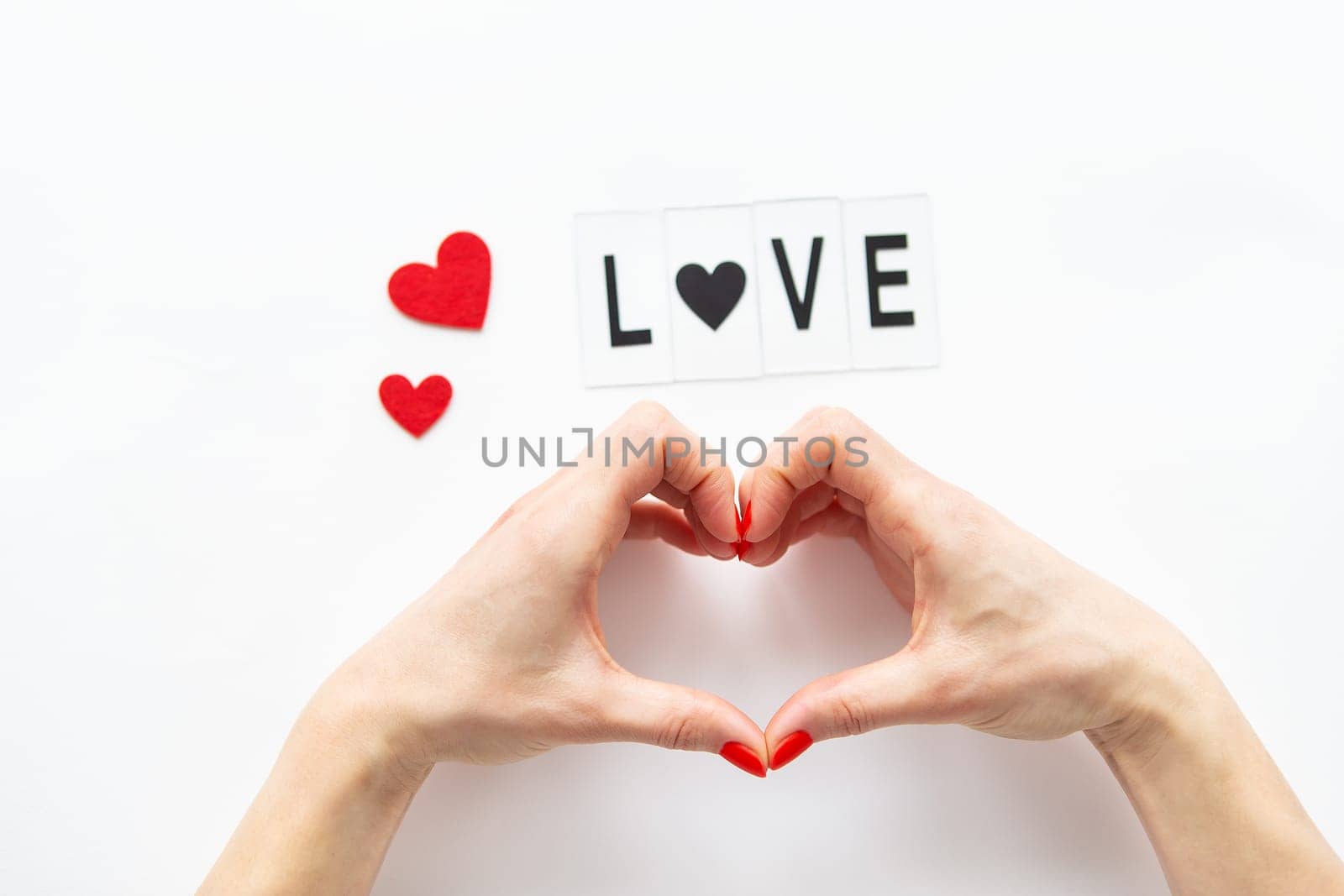 Female hands in the shape of a heart isolated on a white background, side view of small red hearts. Love lettering