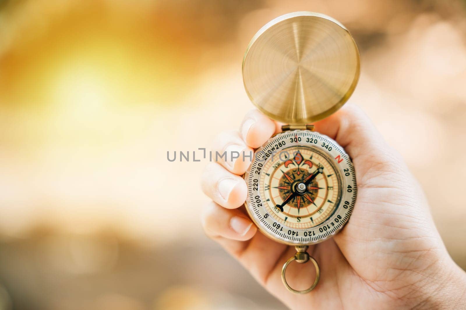 Close-up of hand holding a compass in the midst of a green forest offering ample space for text. Symbolizing guidance and exploration it relates to travel lifestyle and successful business management. by Sorapop