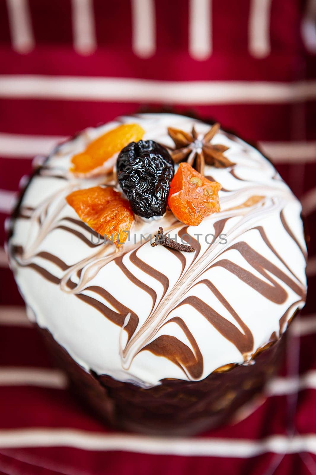 A close-up of a cupcake with white icing, chocolate drizzle, and dried fruits on a striped background. Easter holiday concept. by sfinks