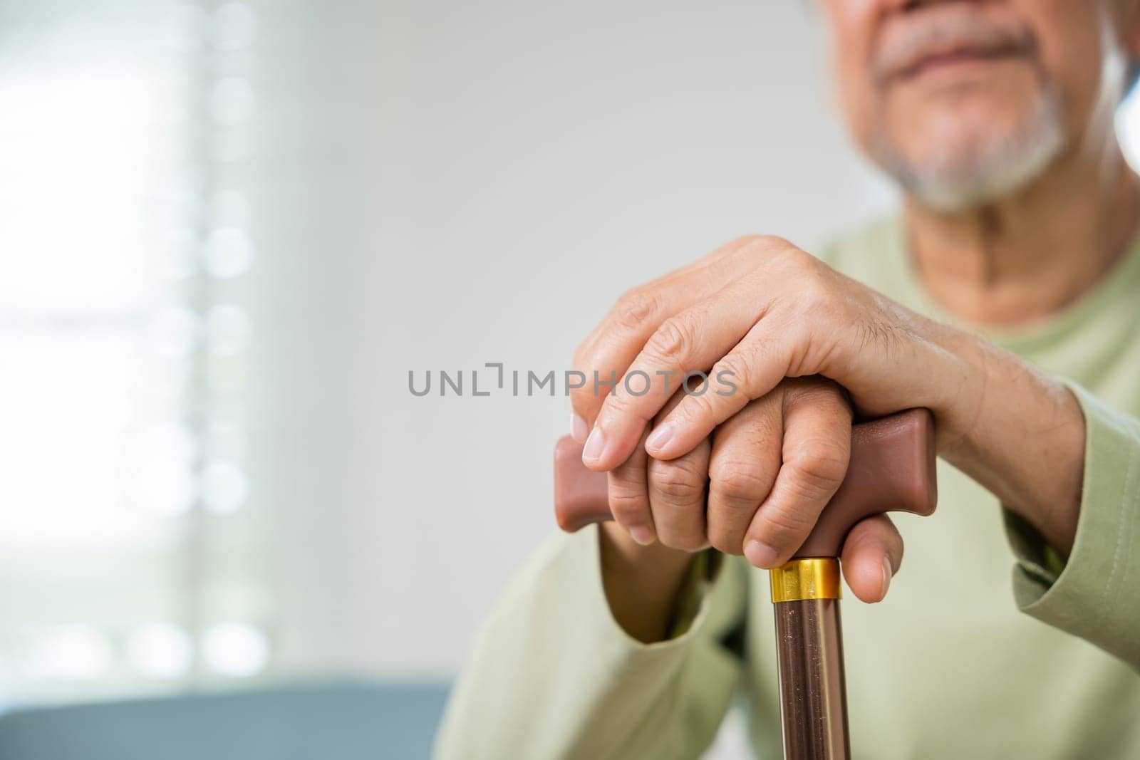 Hands of Asian Old man sitting resting at home hold wooden walking cane by Sorapop