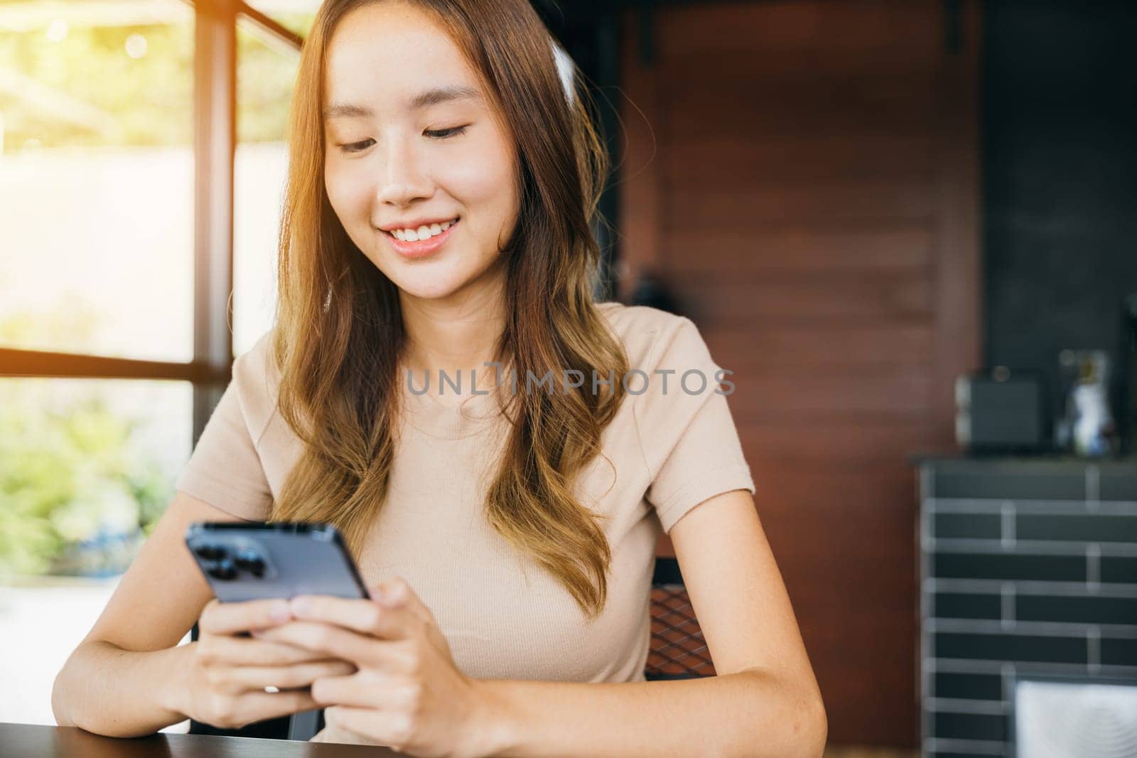 Beautiful Asian female has transfer money financial internet banking on mobile phone, young woman using smart phone for shopping online at cafe coffee shop near windows in the morning