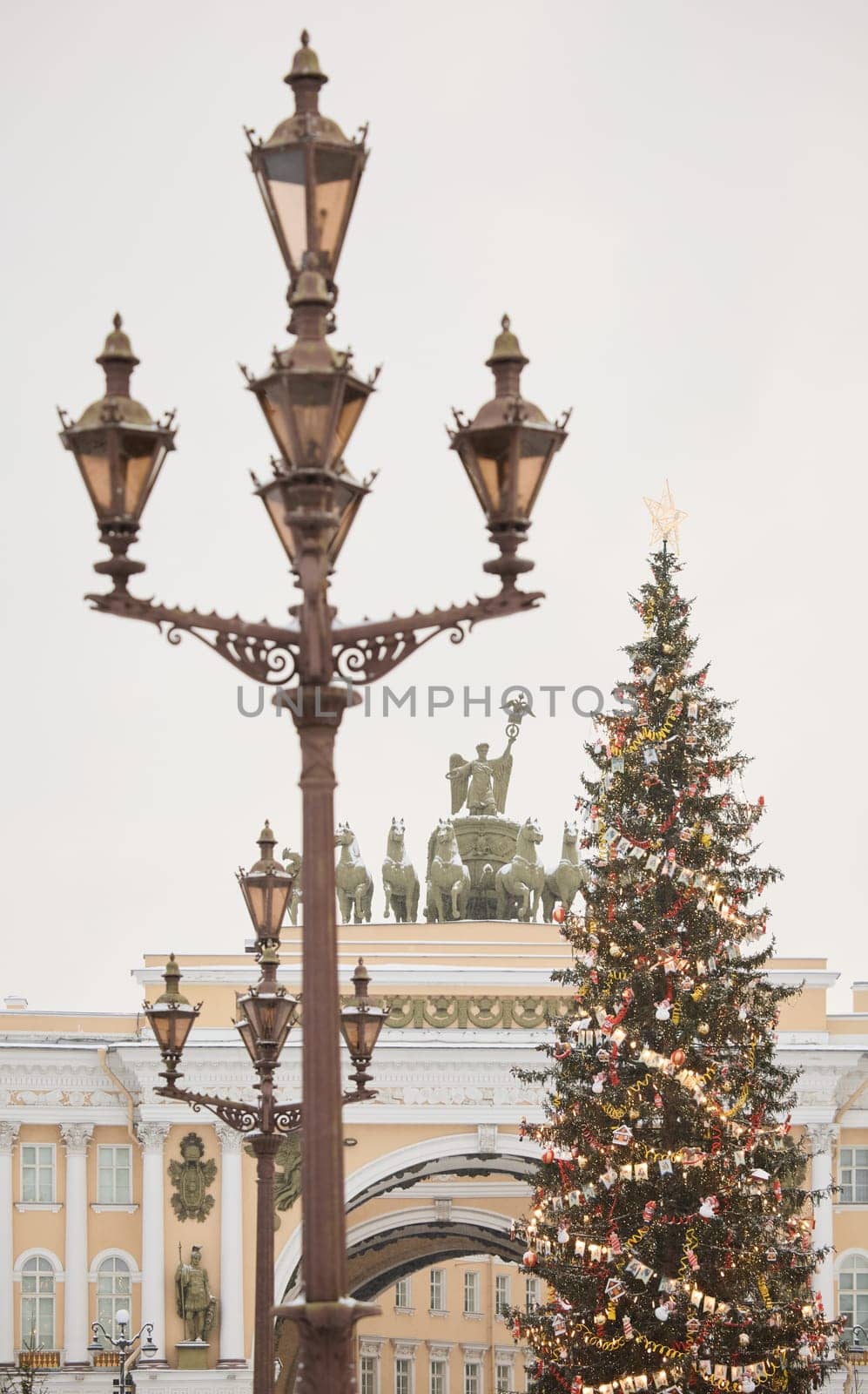 The main Christmas tree shimmers with lights of decorations through vintage lamppost, the central Palace square of the city decorated for the celebration during the snowfall, Arch of the General Staff. High quality photo
