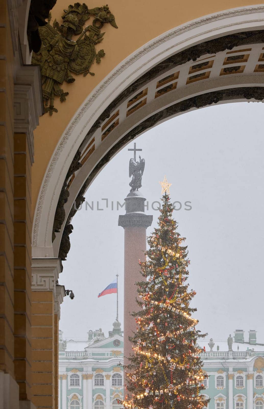 The main Christmas tree shimmers with decorations, Alexander column with angel with cross, the Palace square during the snowfall, national flag of Russia by vladimirdrozdin