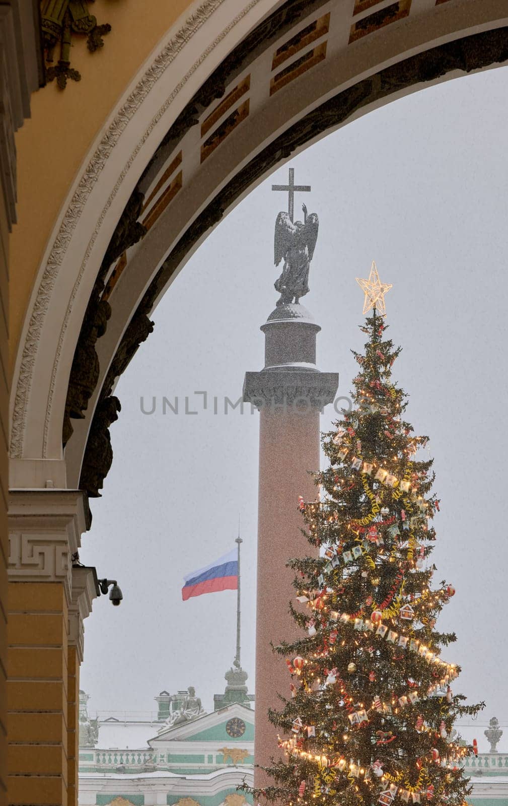 The main Christmas tree shimmers with decorations, Alexander column with angel with cross, the Palace square during the snowfall, national flag of Russia. High quality photo