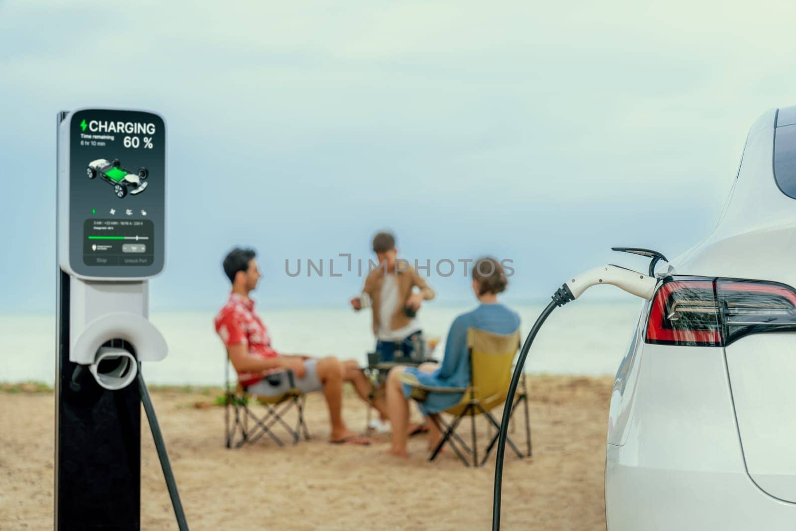 Alternative family vacation trip traveling by the beach with electric car recharging battery from EV charging station with blurred family enjoying the seascape background. Perpetual