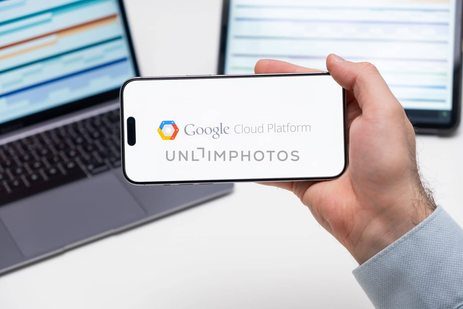 Google Cloud Platform logo of app on the screen of mobile phone held by man in front of the laptop and tablet, December 2023, Prague, Czech Republic