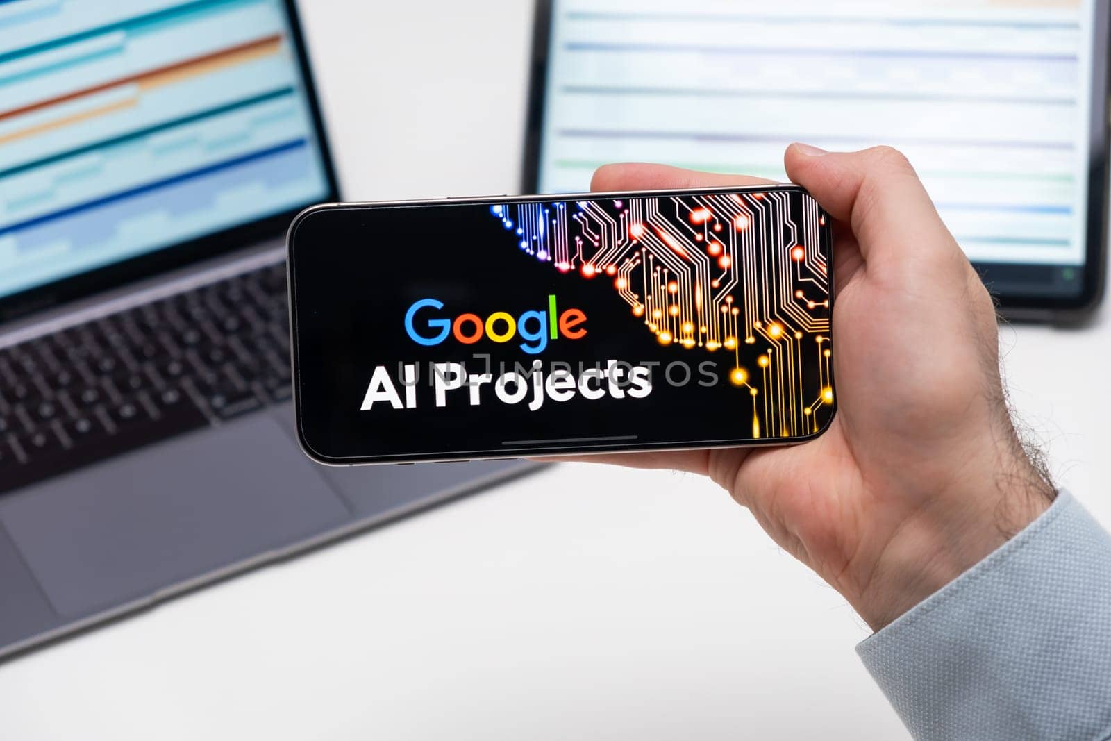 Google AI protects logo of app on the screen of mobile phone held by man in front of the laptop and tablet, December 2023, Prague, Czech Republic