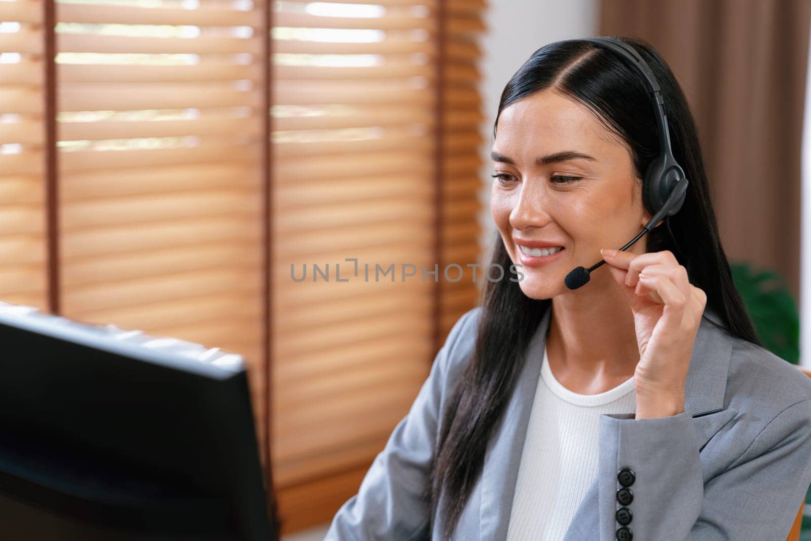 Female call center operator or customer service helpdesk staff working on workspace while talking on the headset to provide assistance for customer. Professional modern business service. Blithe