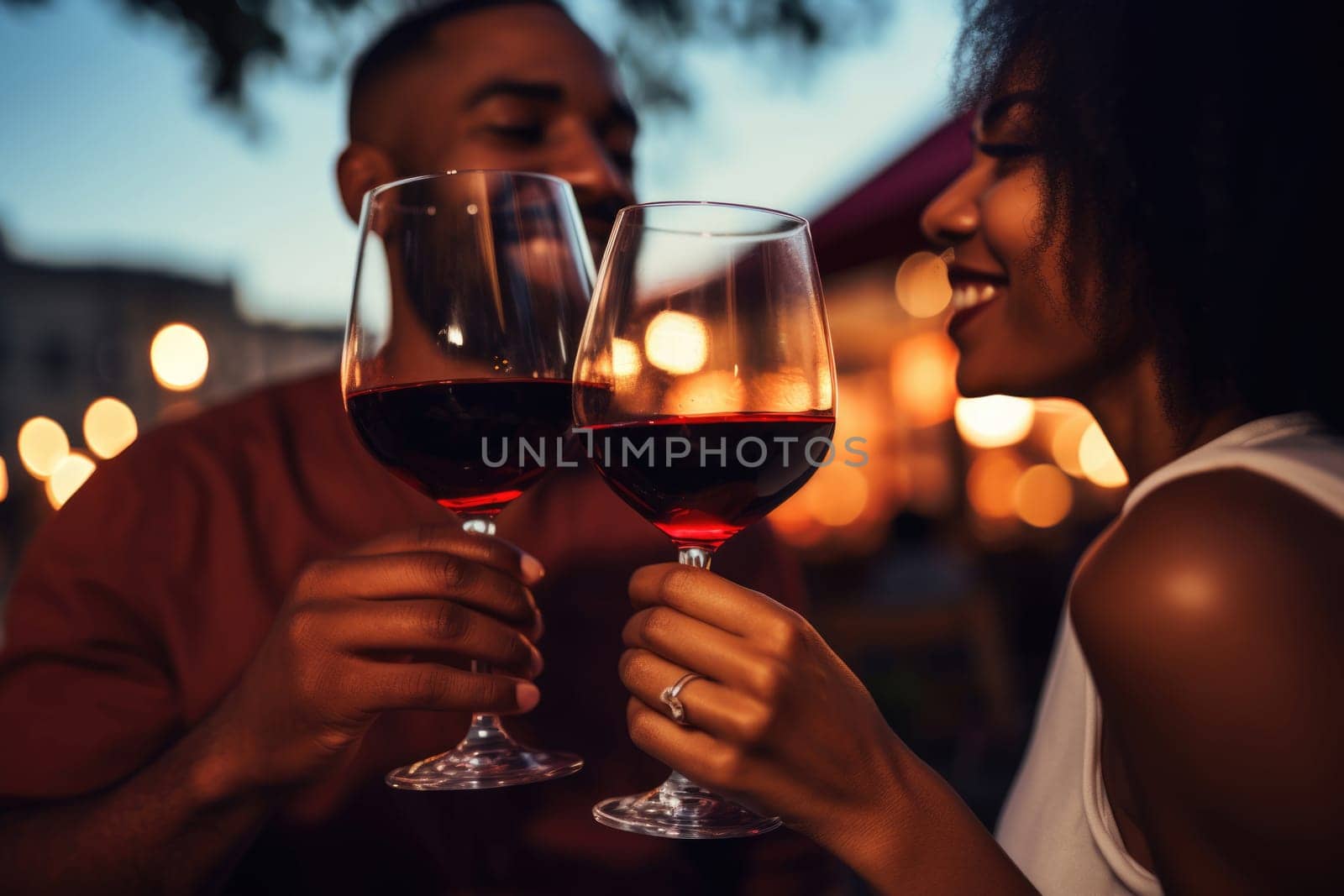 Couple celebrating Valentines day at restaurant with red wine. Close up of happy african american man and woman clinking glasses against blurred outdoor background