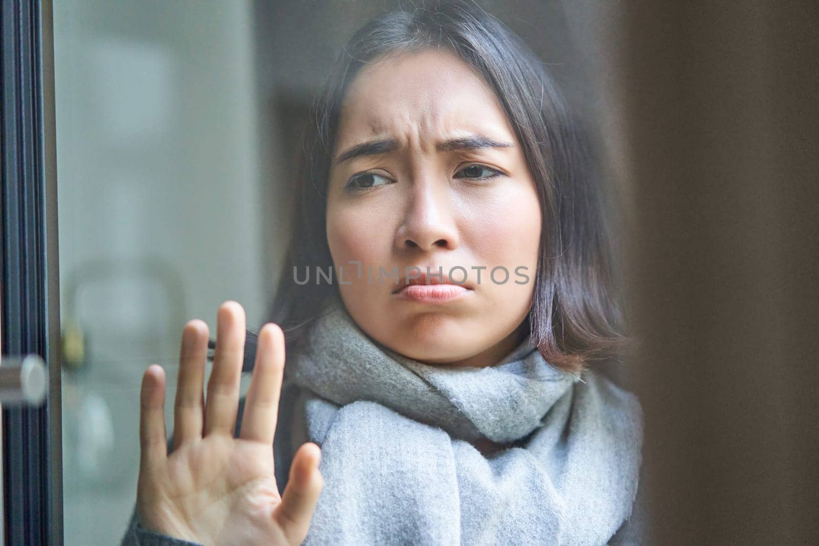 Portrait of sad ill woman staying at home, looking out of the window with jealous and upset face, cant leave home as being sick with covid-19.