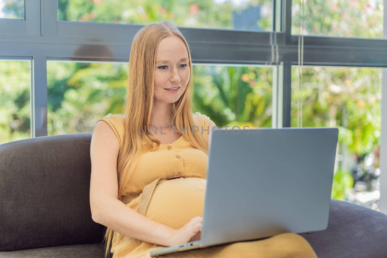 Pregnant woman working on laptop. Expectant woman efficiently works from home during pregnancy, blending professional commitment with maternal duties by galitskaya