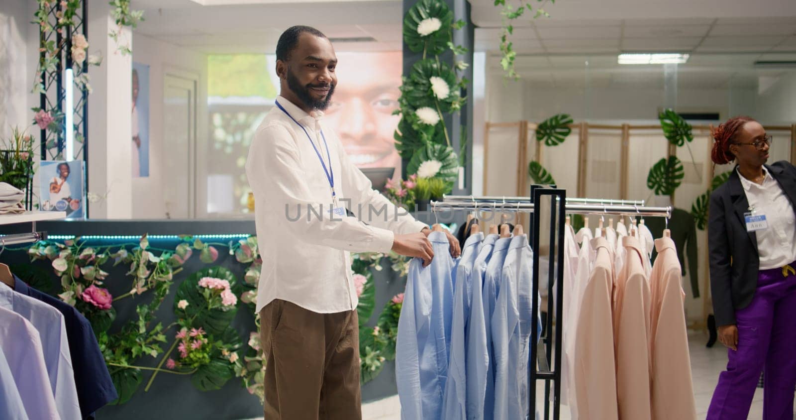 Smiling retail assistant arranging clothes in mall clothing store with fast fashion attire following the latest trends. Cheerful worker organizing assortment of elegant men blazers in fashion boutique