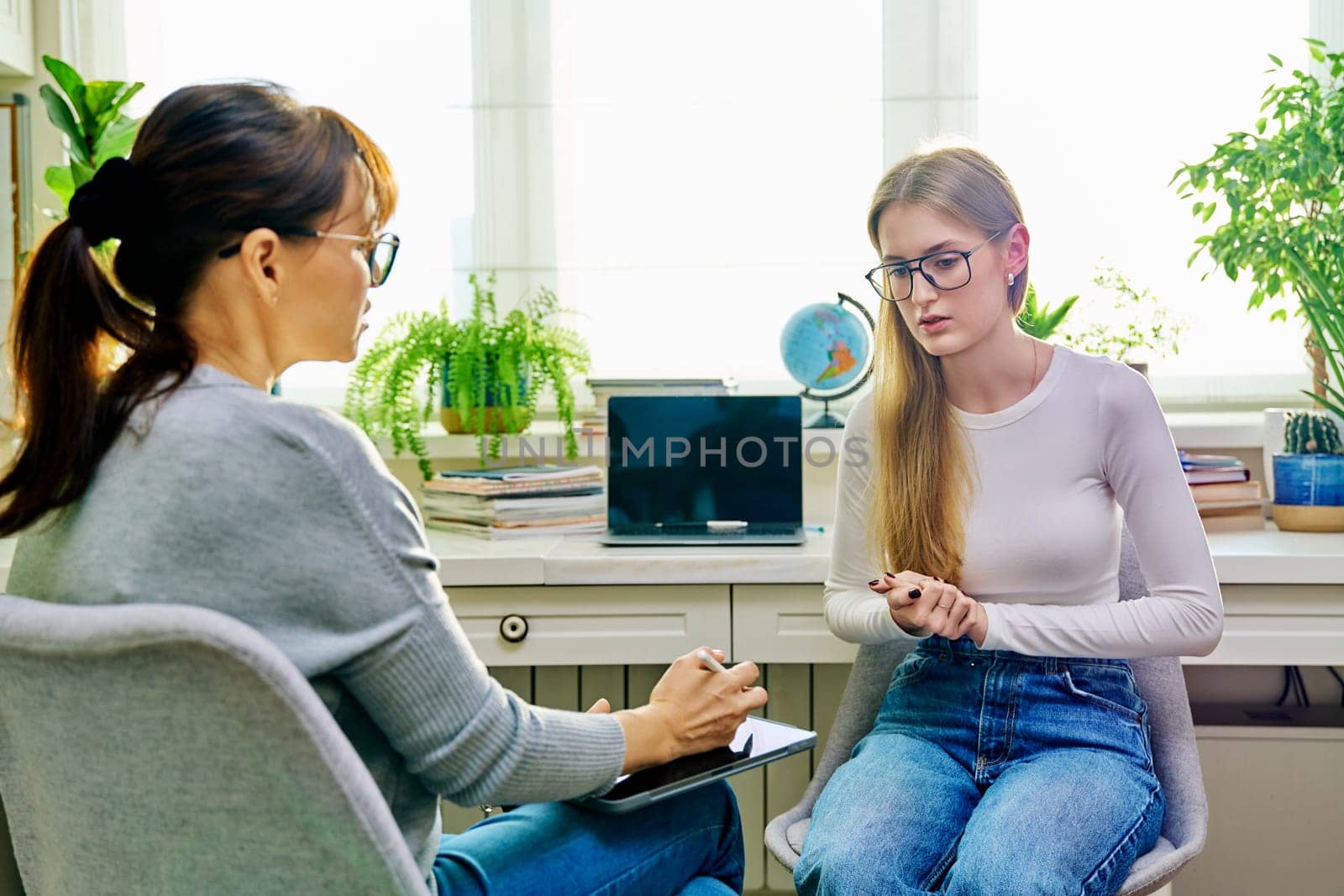 Young female teenager 16, 17 years old talking with counselor psychologist behavior social worker teacher, sitting in chair in office. Psychology psychotherapy therapy mental health adolescence youth