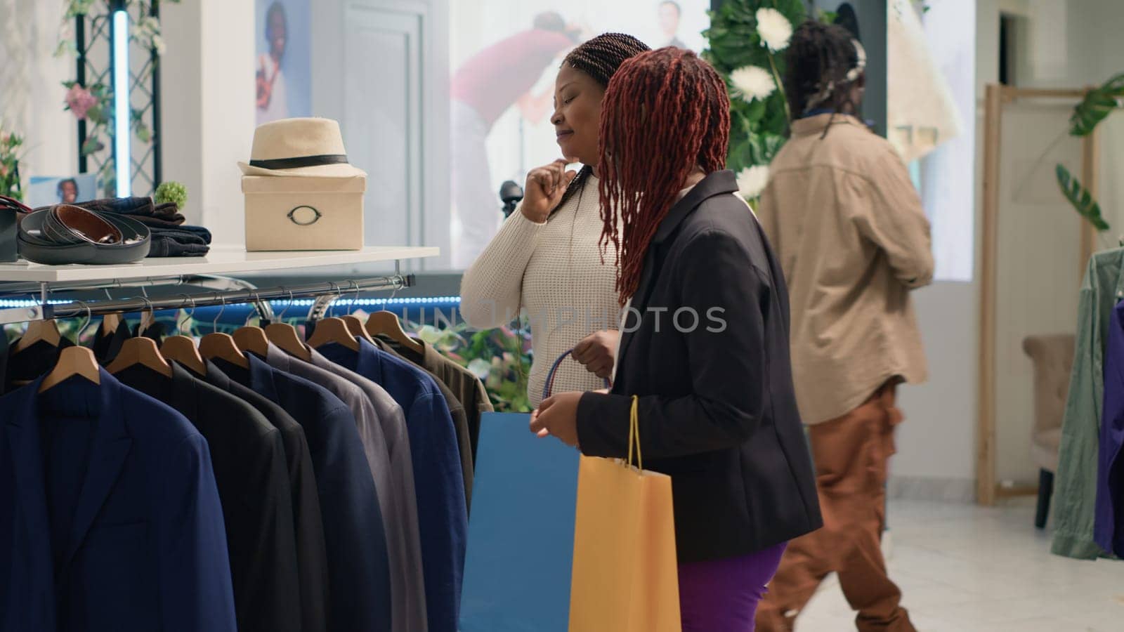 Woman doing purchases together in clothing shop with fashion expert helping her fill wardrobe with stylish clothes. Customer and commissioned specialist with shopping bags in mall boutique