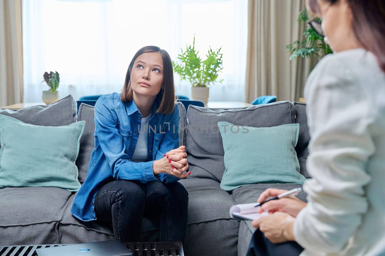 Sad young woman at therapy session with psychologist, psychiatrist. Therapist counselor and unhappy female patient on sofa in office. Psychology counseling treatment psychotherapy mental health youth