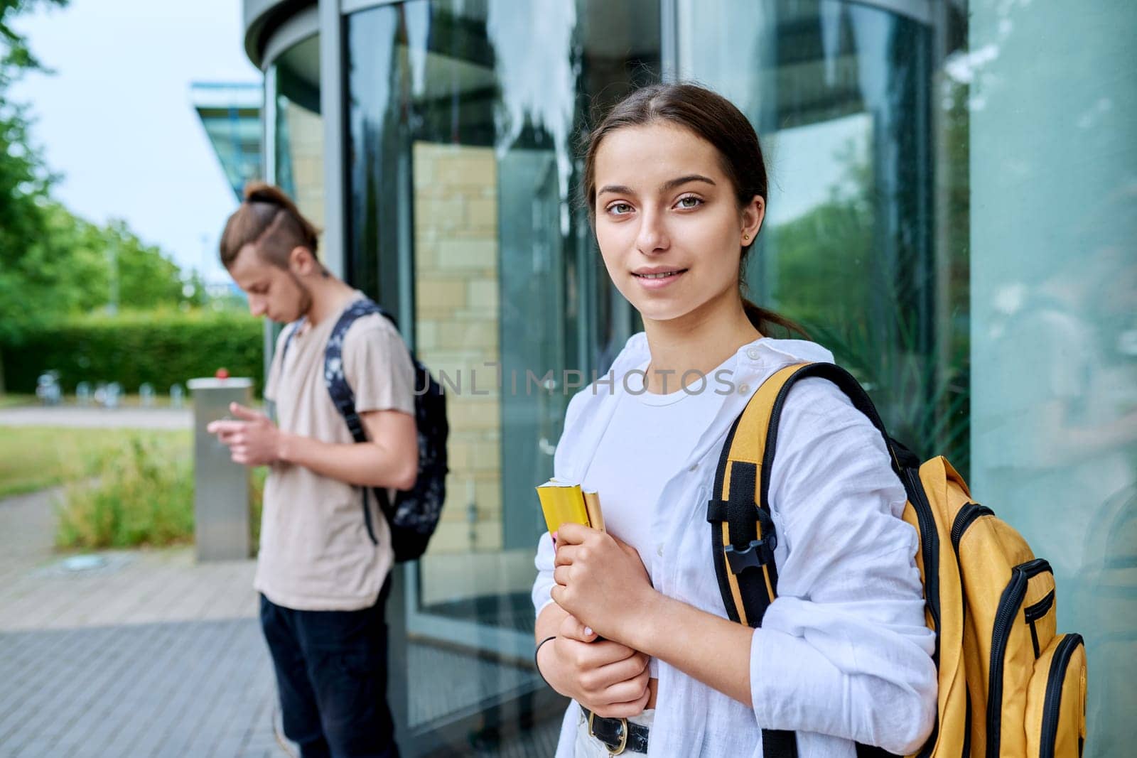 Portrait of high school student, smiling girl with backpack looking at camera, outdoor, educational building background. Adolescence, 15, 16, 17 years old, lifestyle, education concept