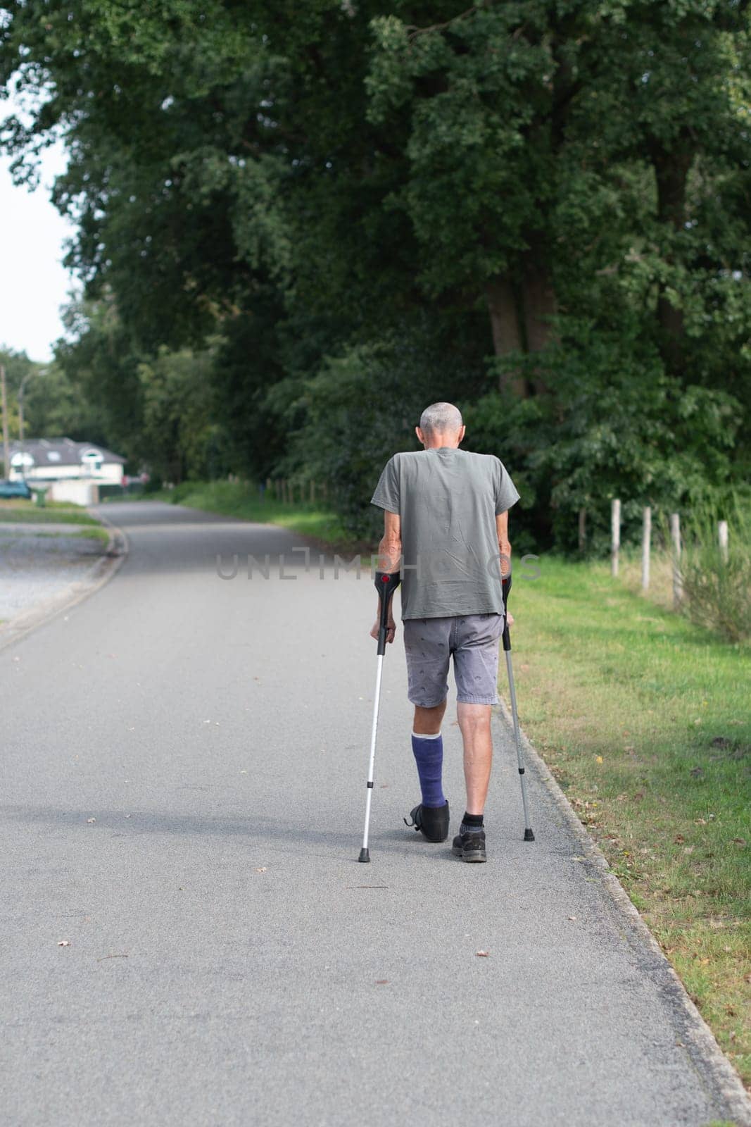 A man with a broken leg is walking down the street, on his left leg he has a special boot for walking, if the leg is in a cast, the man moves with the help of crutches,high quality photo