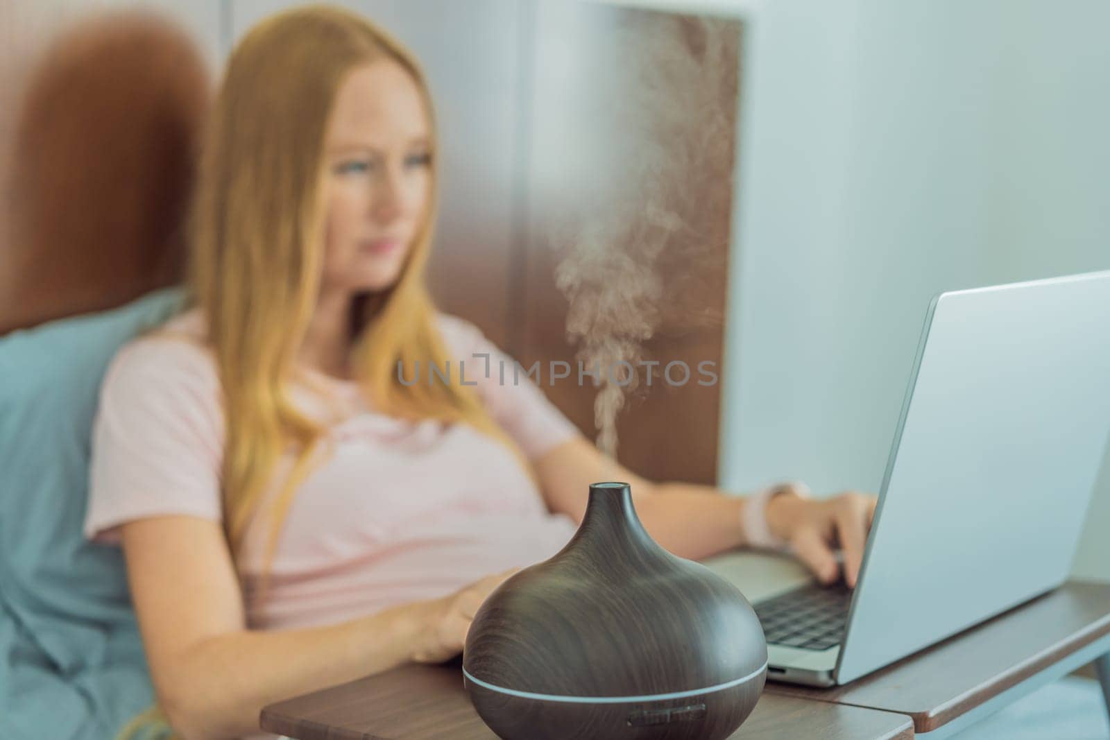 Multitasking expectant woman enhances her home workspace, using an aroma diffuser for a soothing atmosphere while working during pregnancy by galitskaya