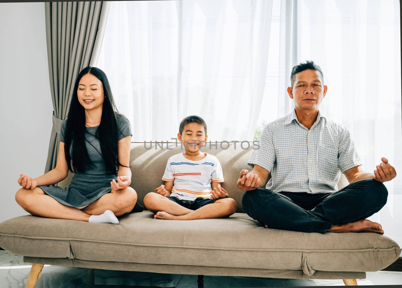 Serene family bonding, parents and their little son practice yoga seated in lotus pose on a sofa. Encouraging harmony balance and tranquility within the home.