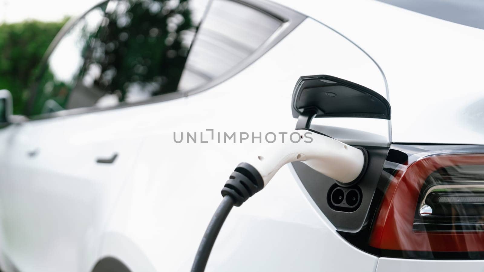 Closeup EV charger plug handle attached to electric vehicle port, recharging battery from charging station. Modern designed EV car and clean energy sustainability for better future concept. Synchronos