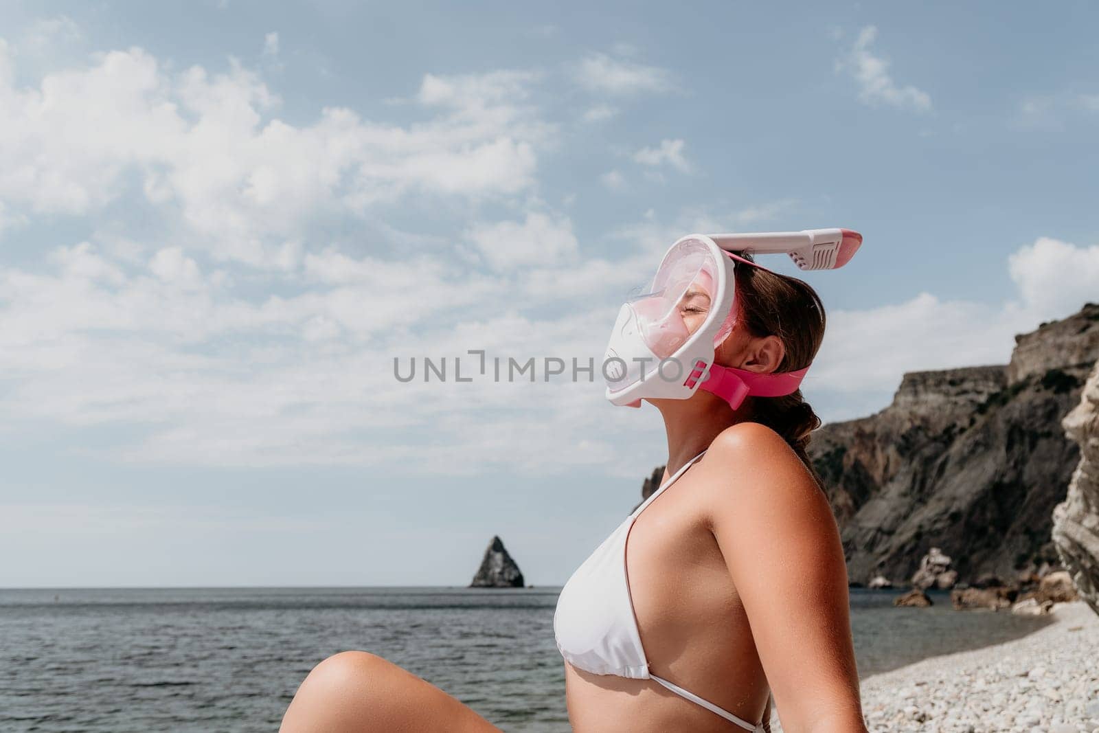 Young happy woman in white bikini put pink snorkeling mask on beach before swimming. girl having fun relaxing on beautiful beach. Beach lifestyle