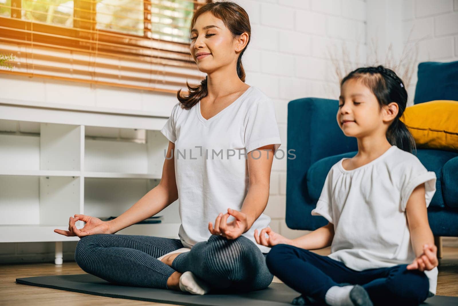 family moment a mother and her little daughter meditate and practice yoga in lotus pose by Sorapop