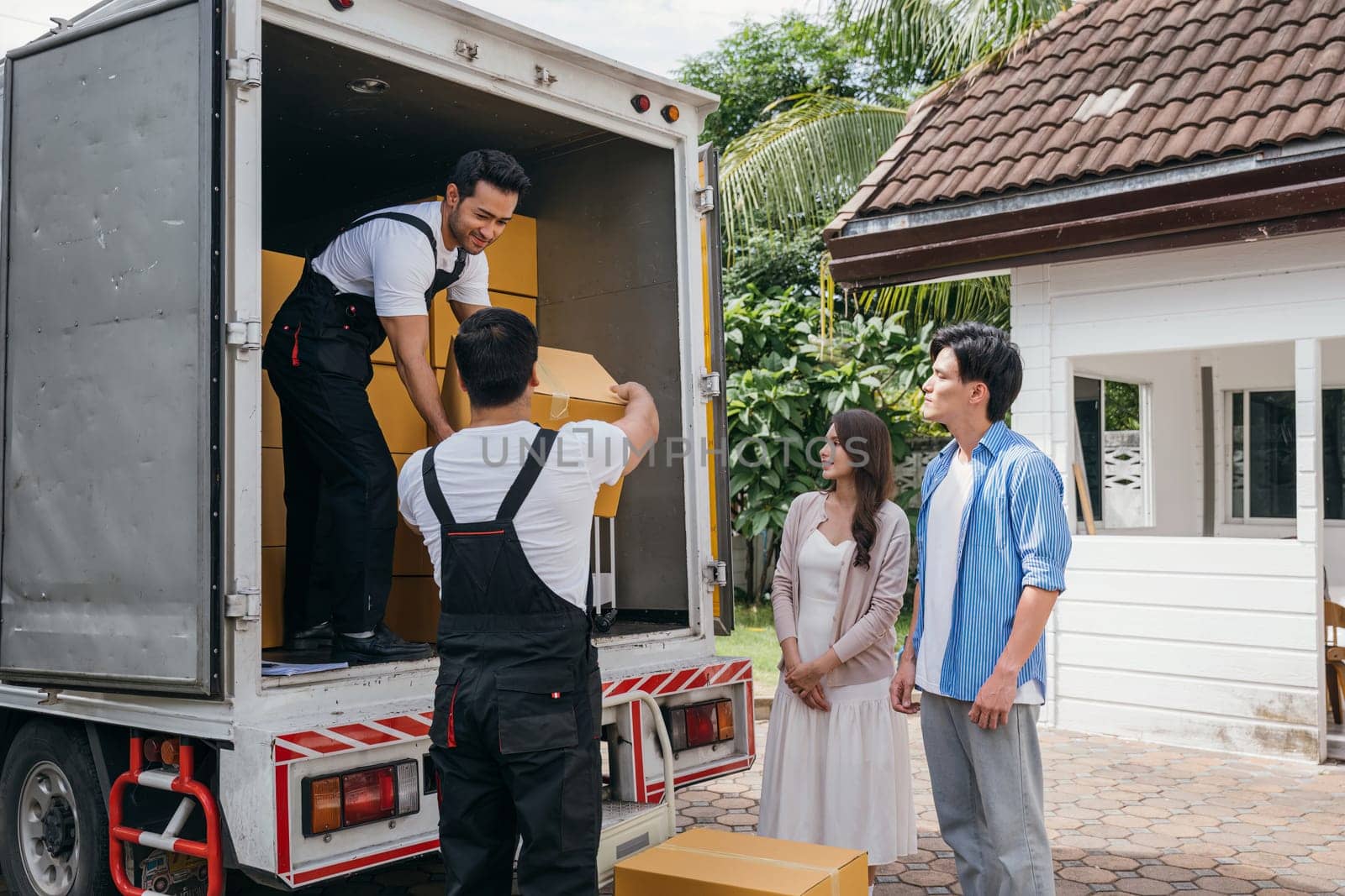 Employees work in unison to help a couple relocate to their new home. They efficiently unload and lift cardboard boxes providing top-notch delivery service. Moving Day Concept