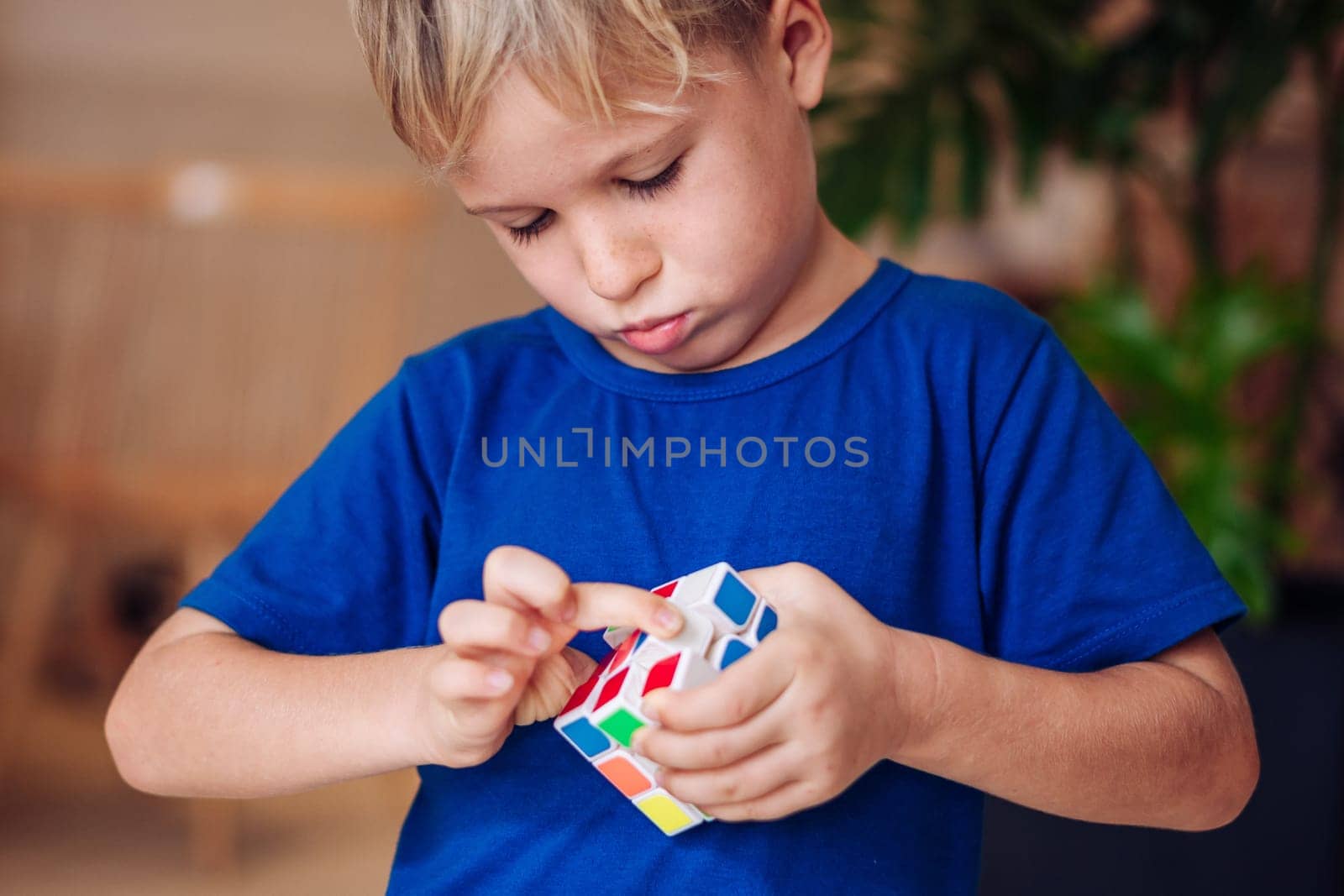 Thoughtful serious inquisitive boy try to complete the rubik's cube. Game childhood development.