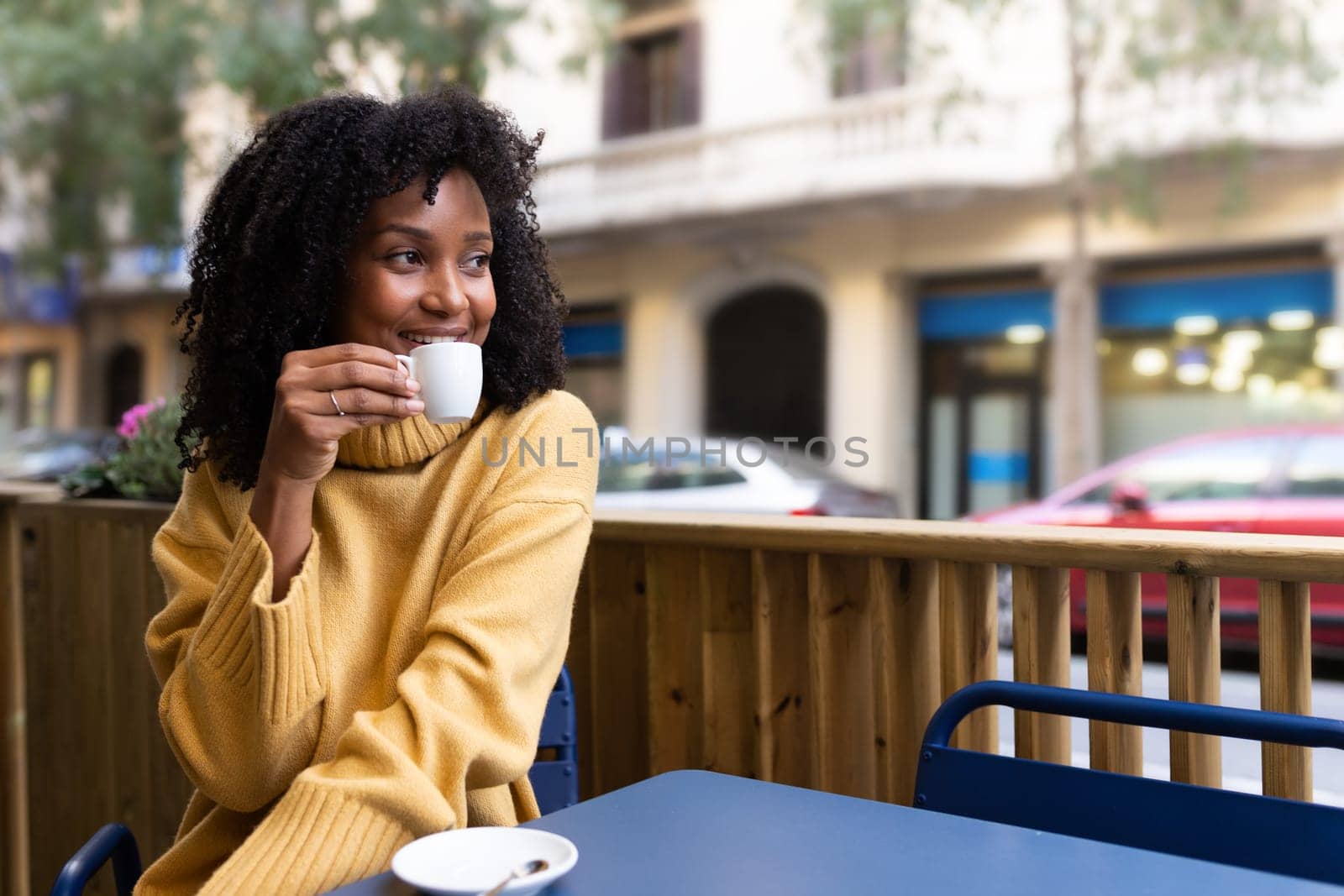 Smiling African American woman drinking espresso coffee in outdoors cafe terrace in the city. Copy space. Lifestyle concept.