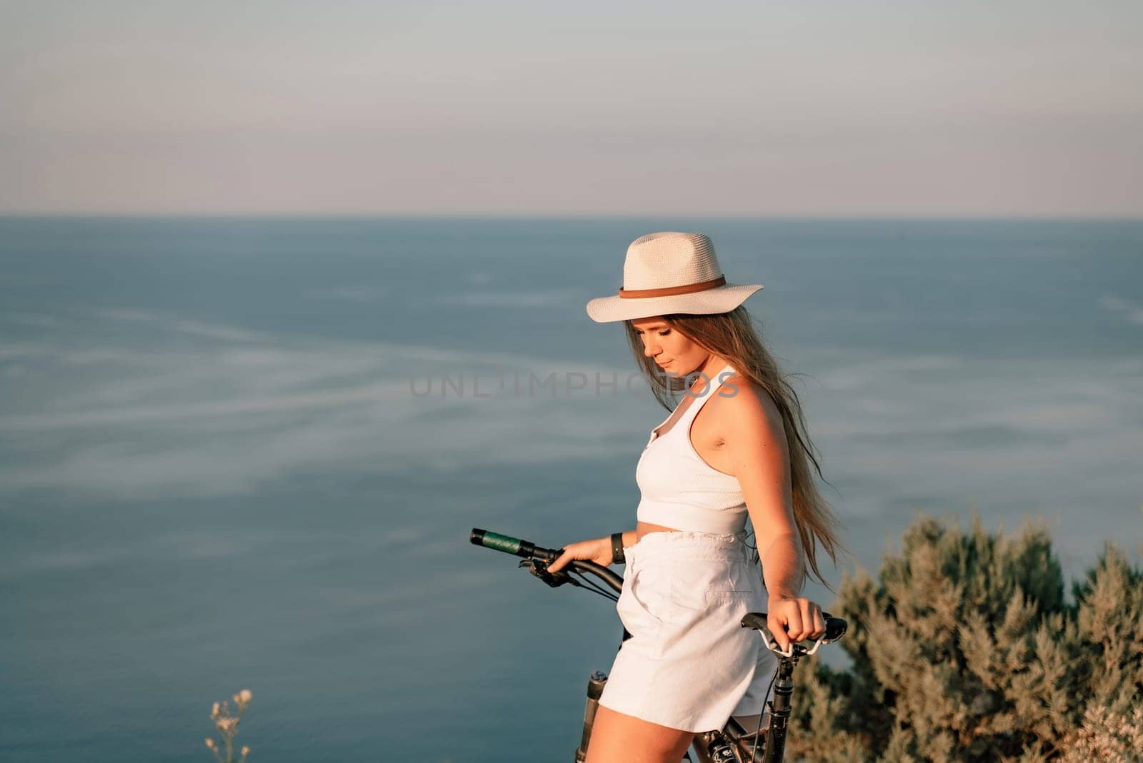 A woman cyclist on a mountain bike looking at the landscape sea. Adventure travel on bike. by Matiunina