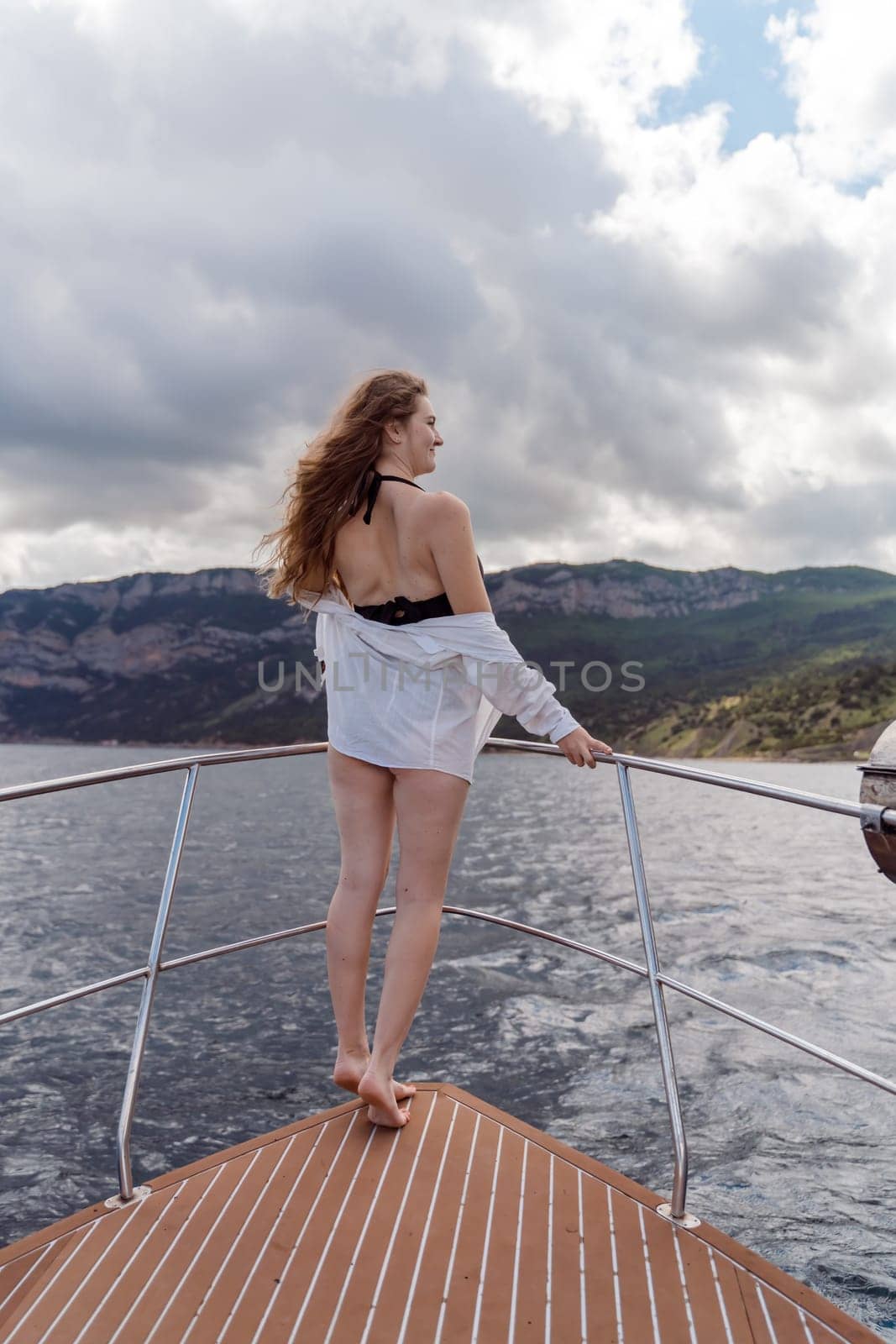 Woman on a yacht. Happy model in a swimsuit posing on a yacht against a blue sky with clouds and mountains.