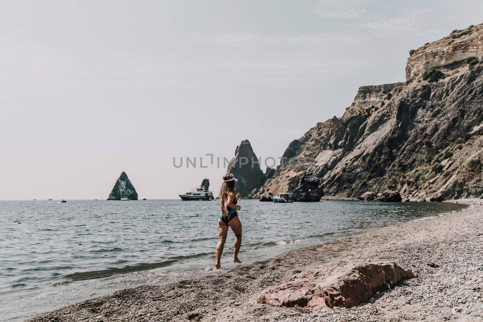 Woman beach vacation photo. A happy tourist in a blue bikini enjoying the scenic view of the sea and volcanic mountains while taking pictures to capture the memories of her travel adventure