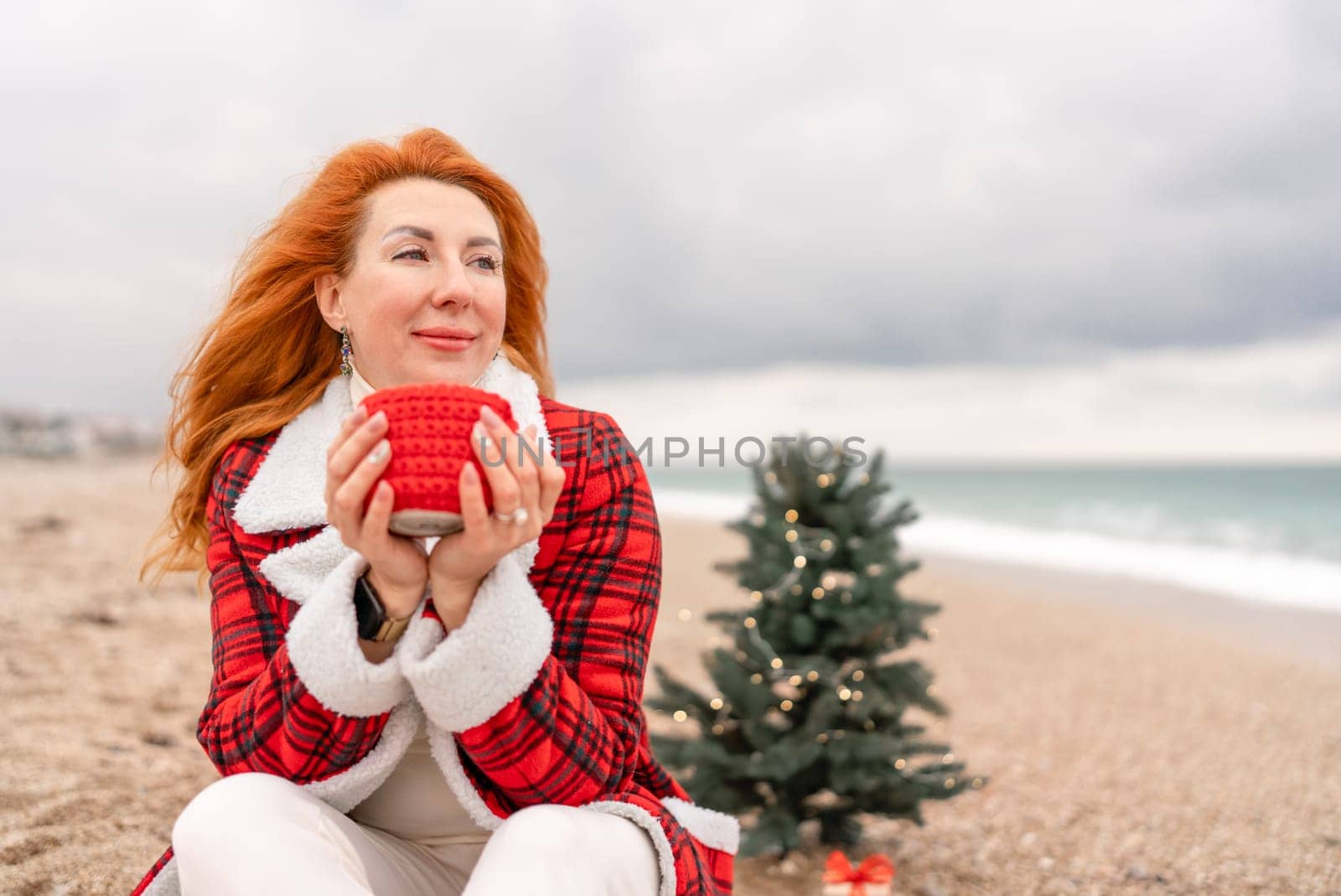 Lady in plaid shirt with a red mug in her hands enjoys beach with Christmas tree. Coastal area. Christmas, New Year holidays concep.
