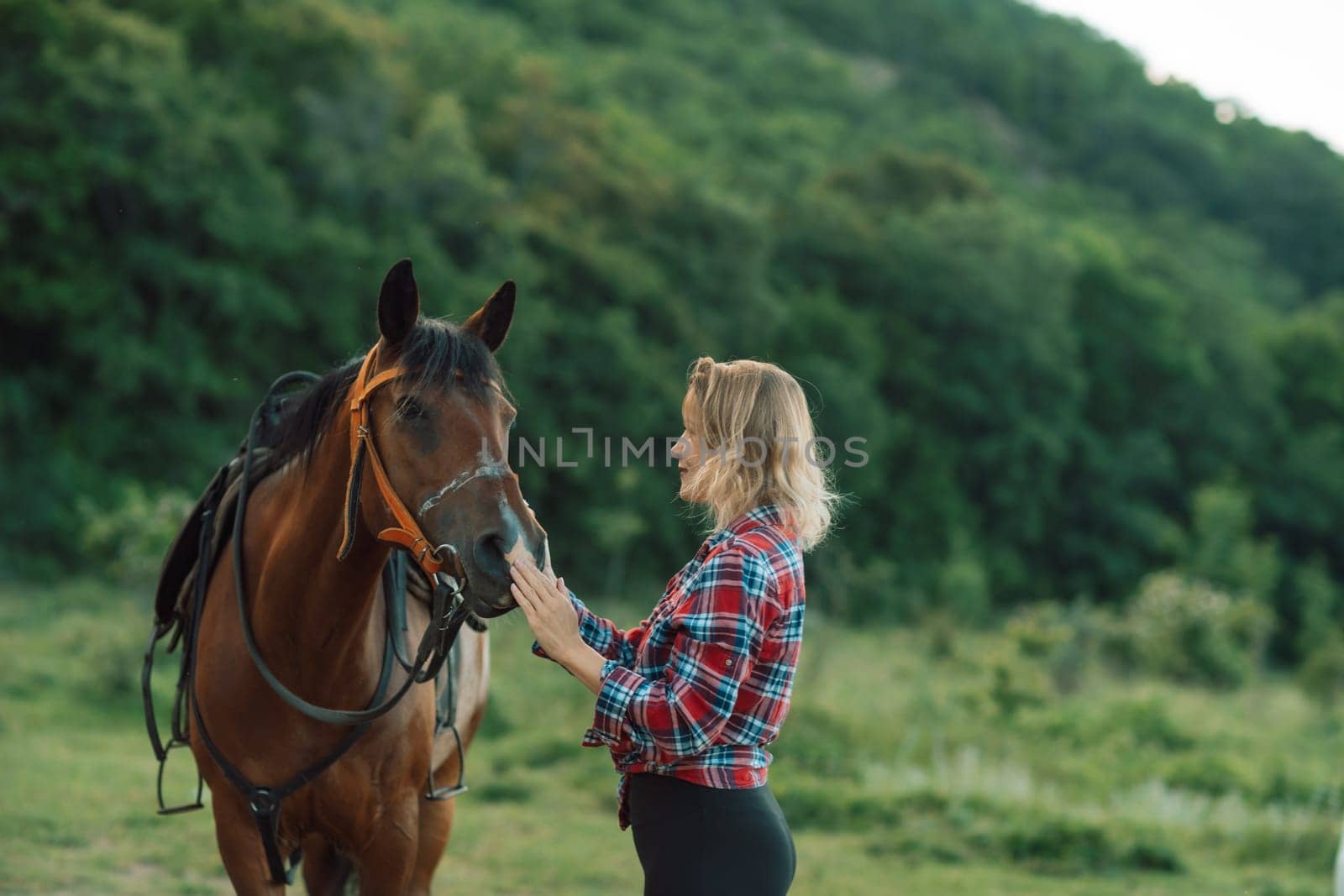 Happy blonde with horse in forest. Woman and a horse walking through the field during the day. Dressed in a plaid shirt and black leggings. by Matiunina
