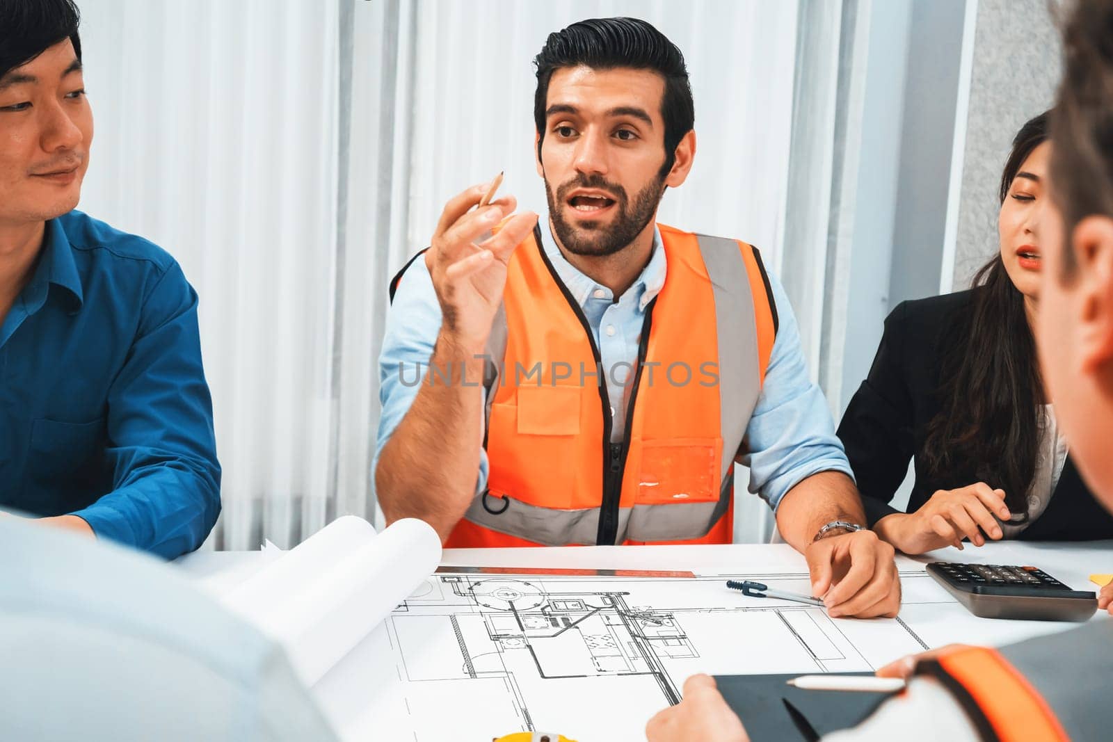 Diverse group of civil engineer and client working together on architectural project, reviewing construction plan and building blueprint at meeting table. Prudent